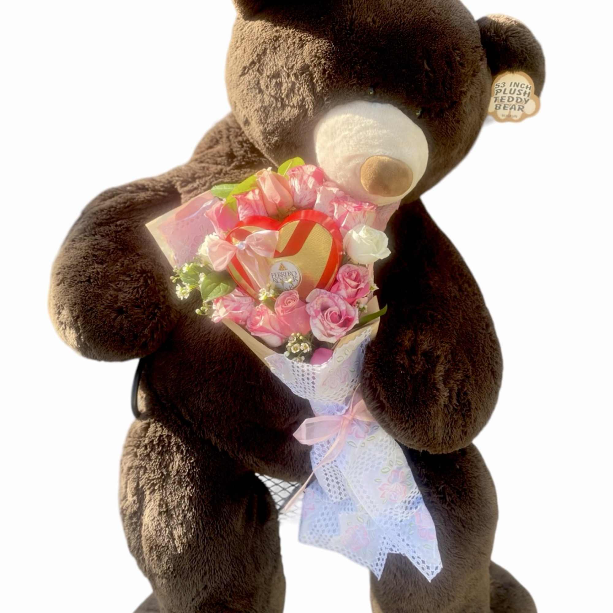 Brown teddy bear holding a pink rose bouquet with a heart box