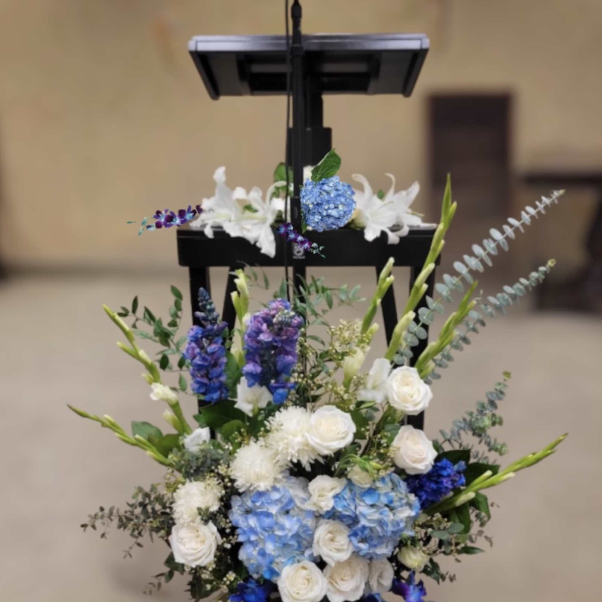 Tall floral arrangement with blue hydrangeas, white roses, and purple blooms on a stand