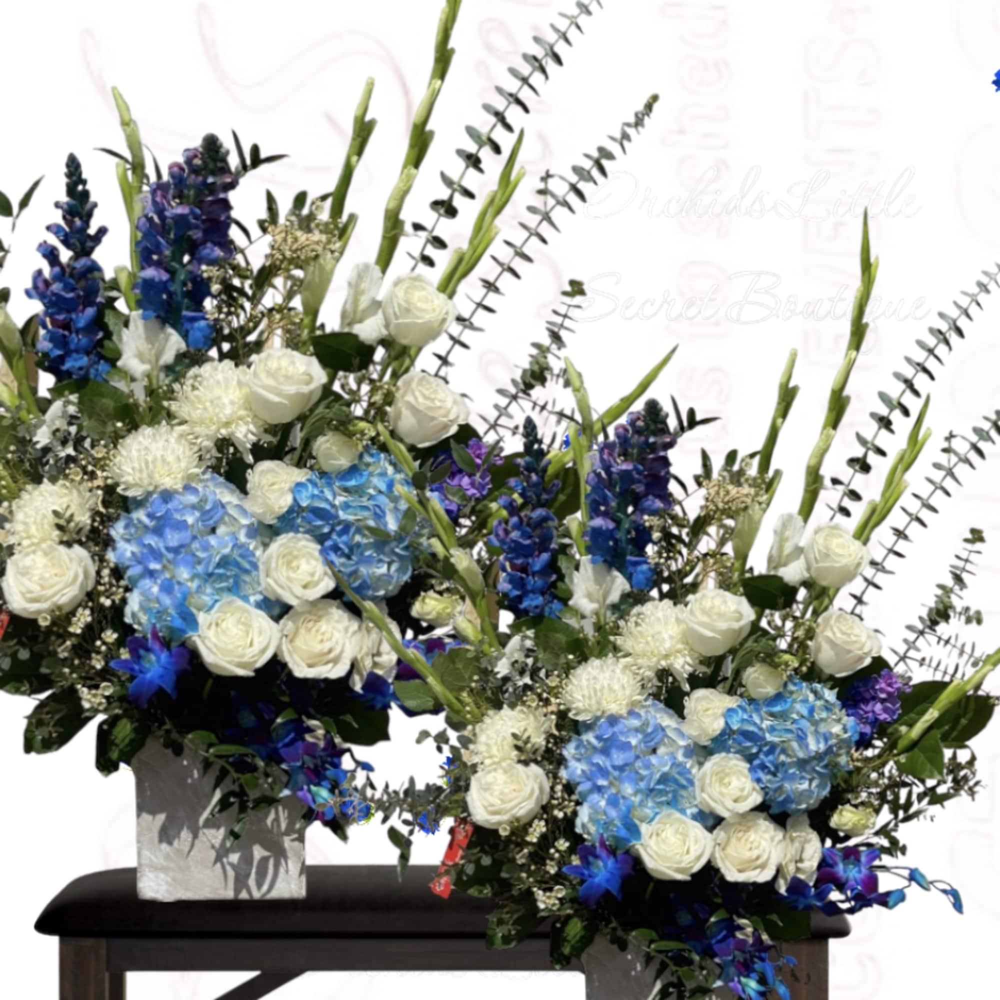 Two tall floral arrangements with blue hydrangeas and white roses in square vases