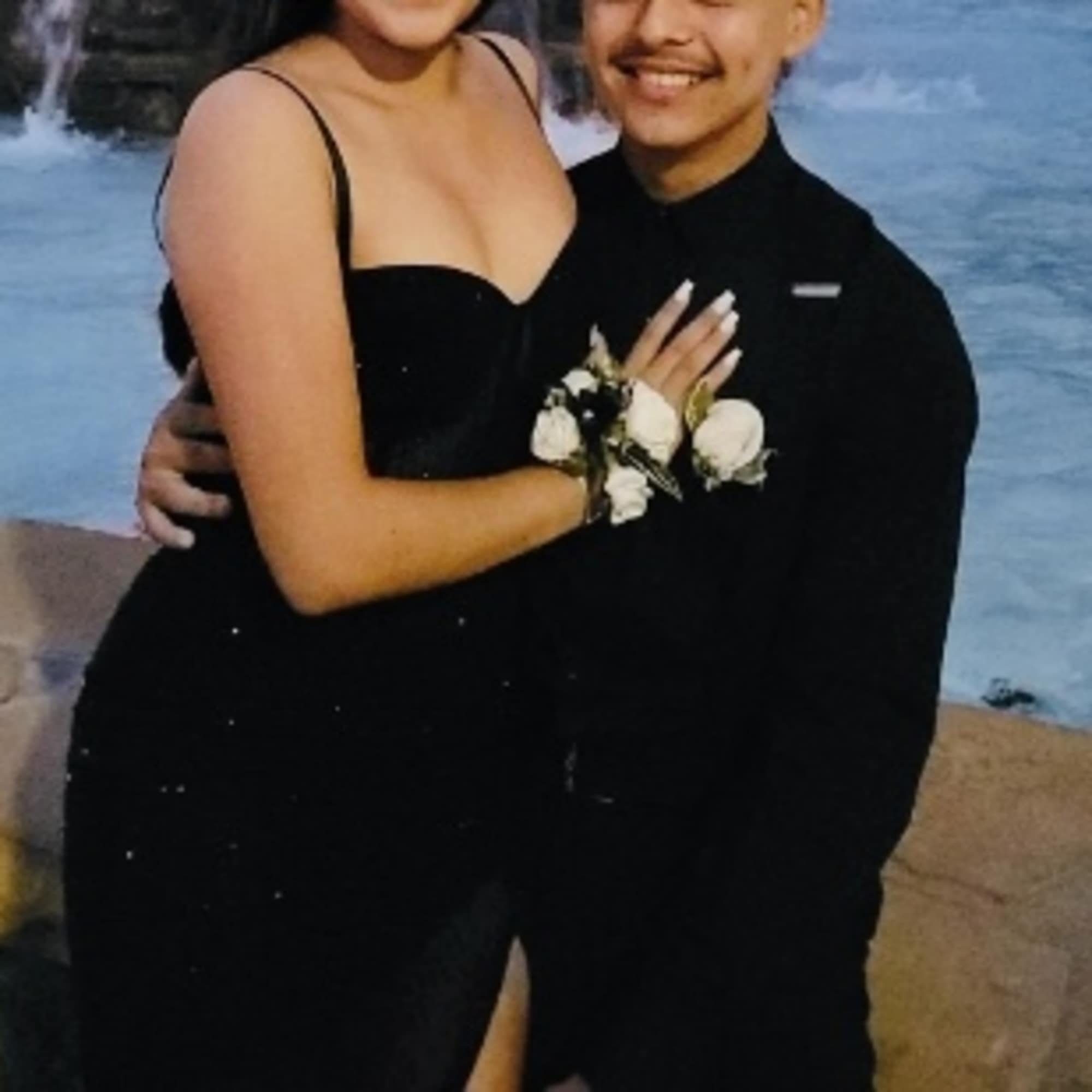 Couple in black formalwear with a small white floral corsage