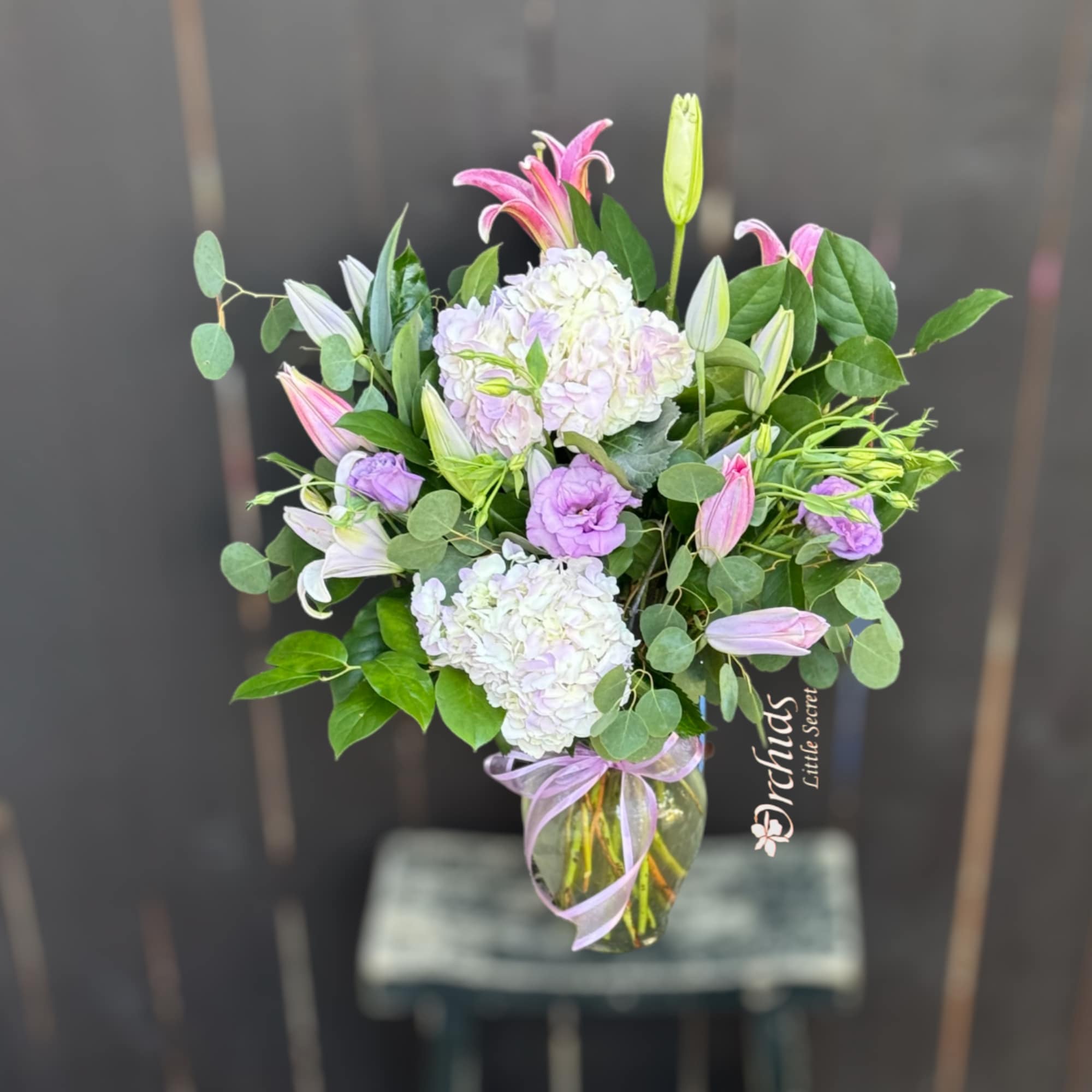 Pink lilies and lavender blooms in a glass vase with ribbon