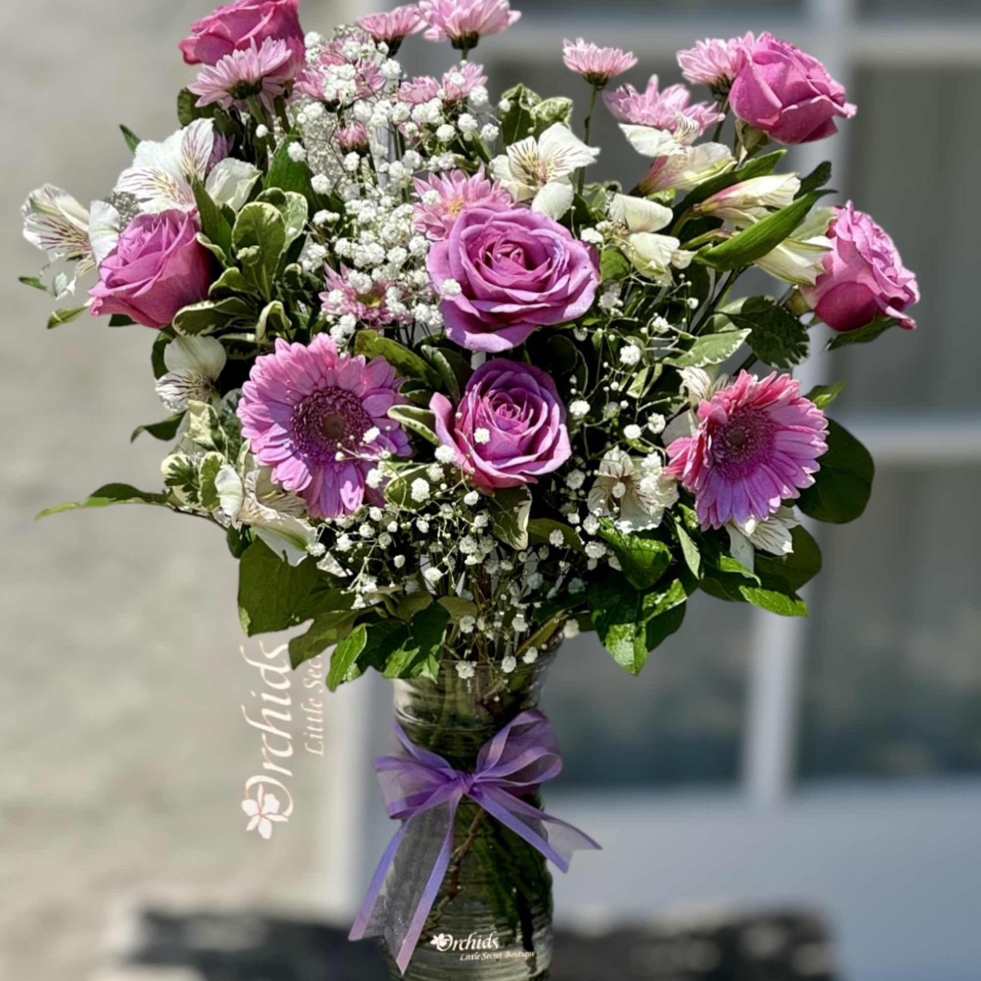 Pink and white mixed bouquet in a glass vase with a purple ribbon