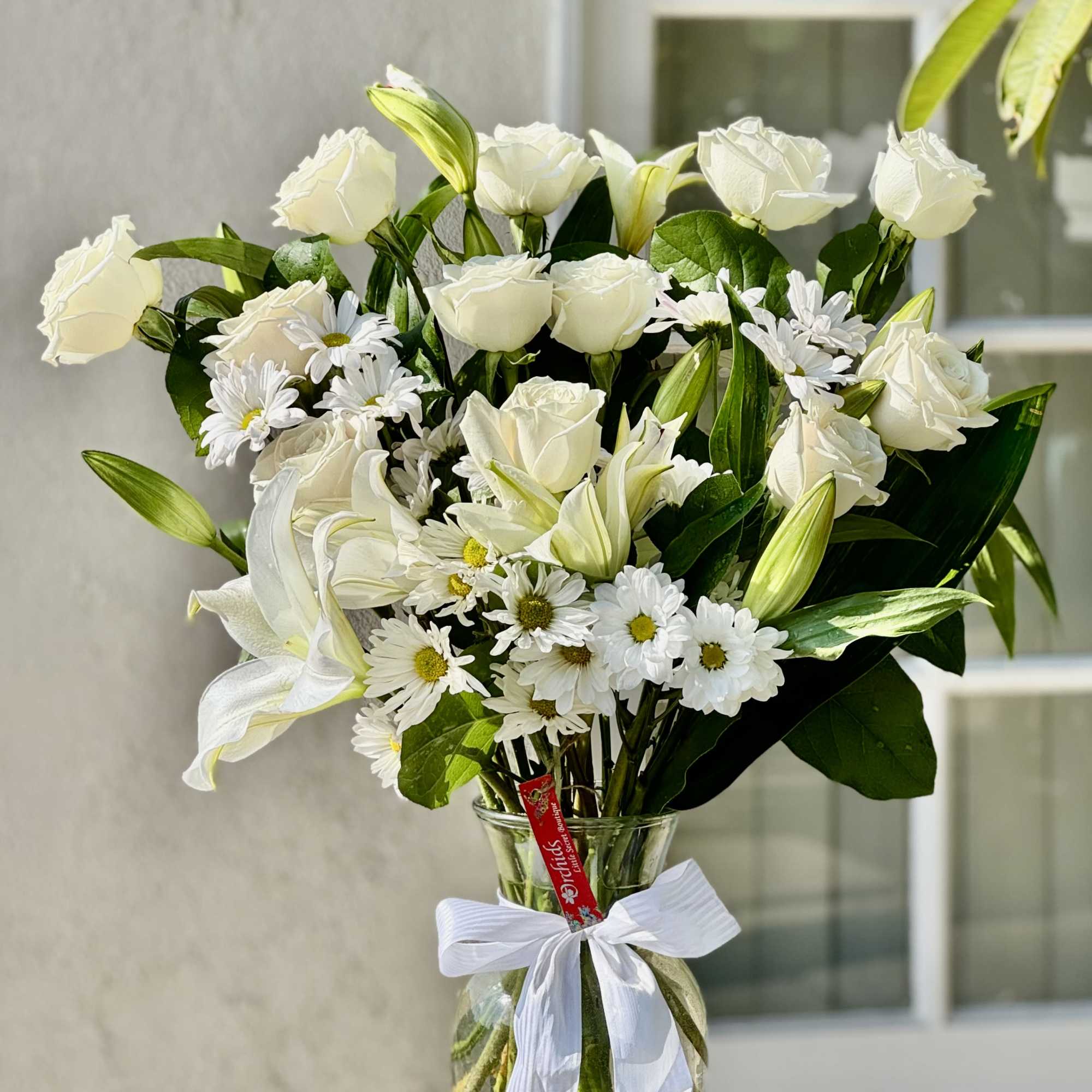 White roses and lilies in a glass vase with a white ribbon