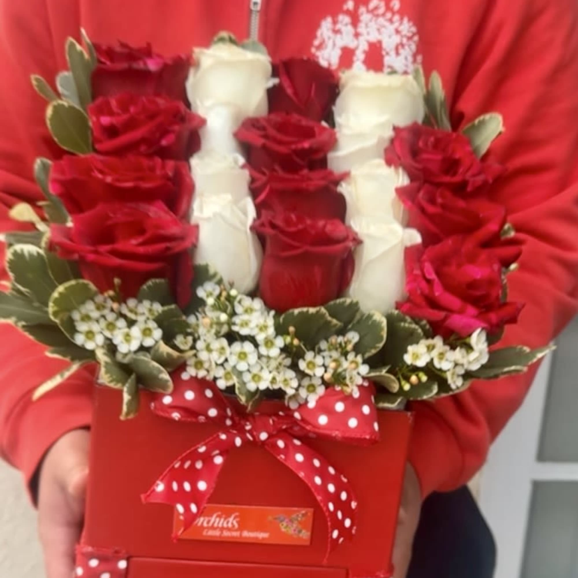 Red and white roses arranged in a red gift box with a polka-dot ribbon.