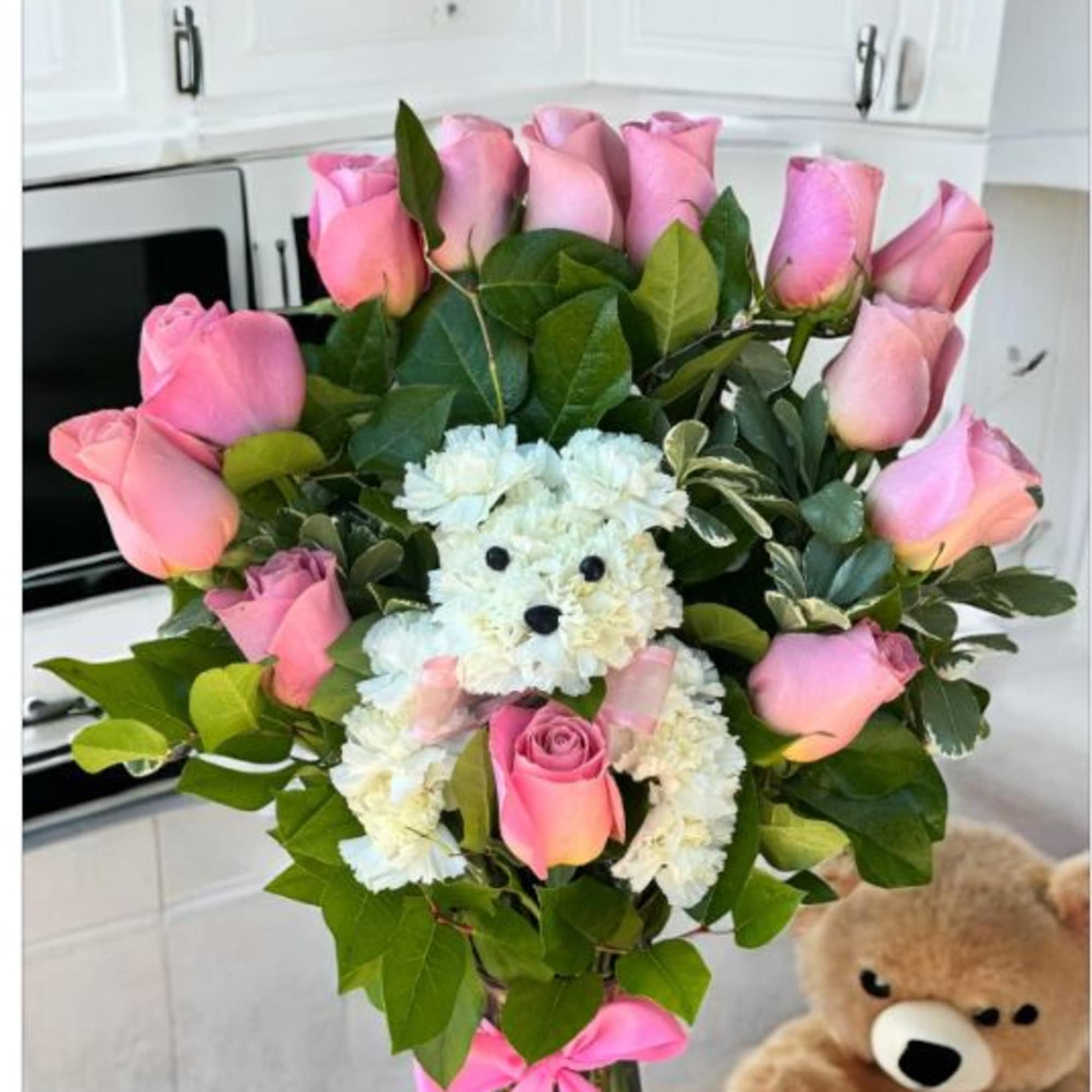 Pink roses and white flowers arranged with a teddy bear in a glass vase