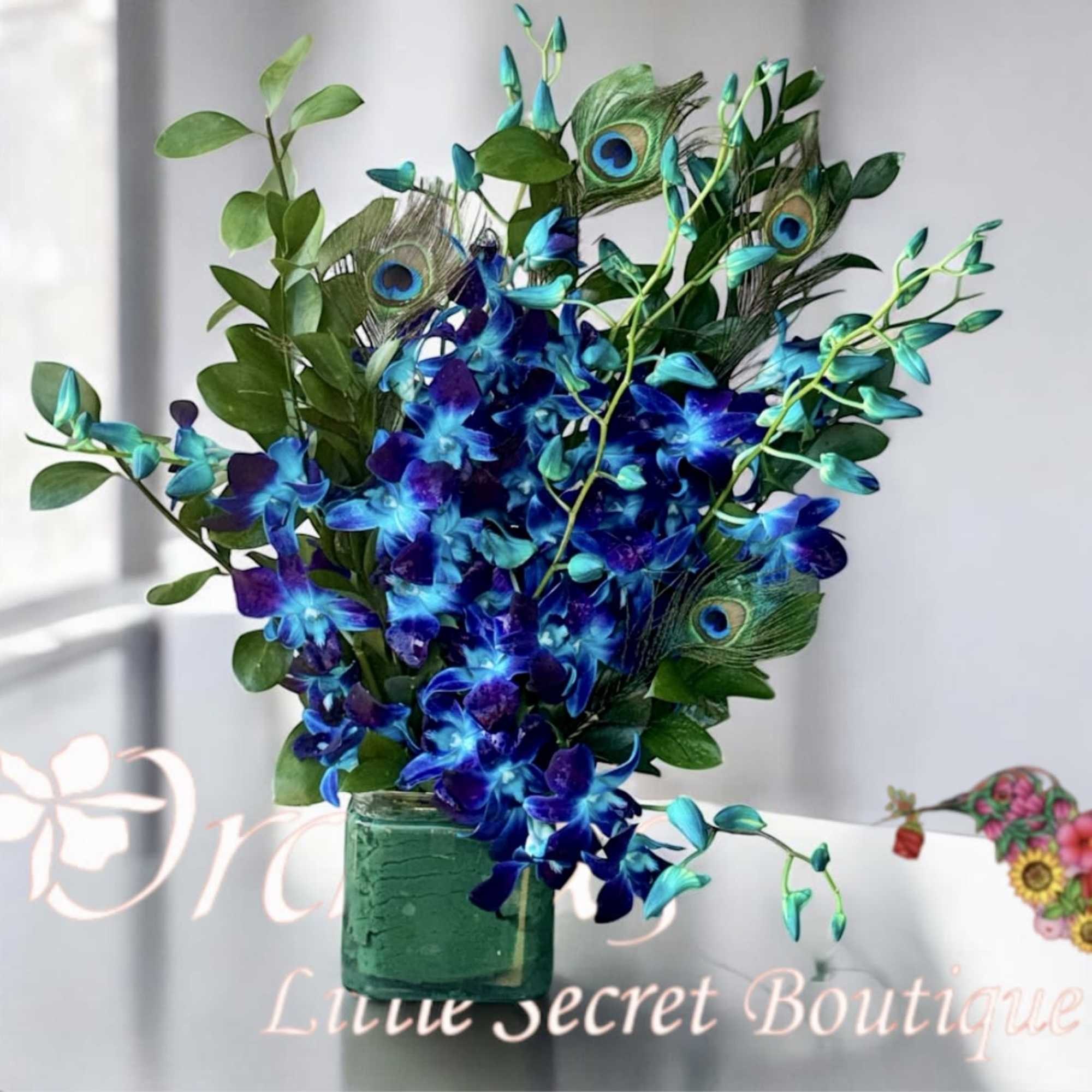 Blue orchid arrangement in a green glass vase with peacock feathers