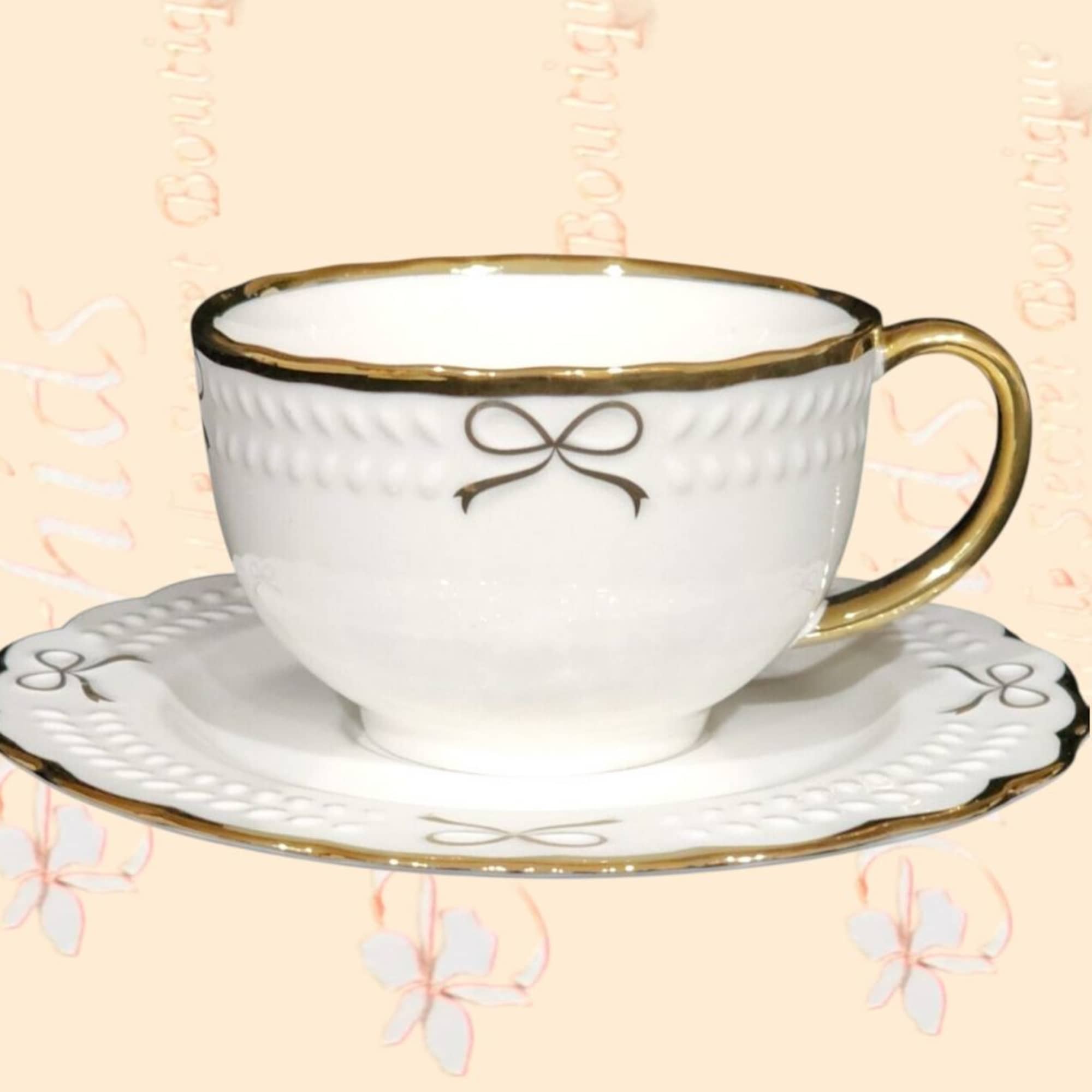 White teacup and saucer with gold trim and a bow motif