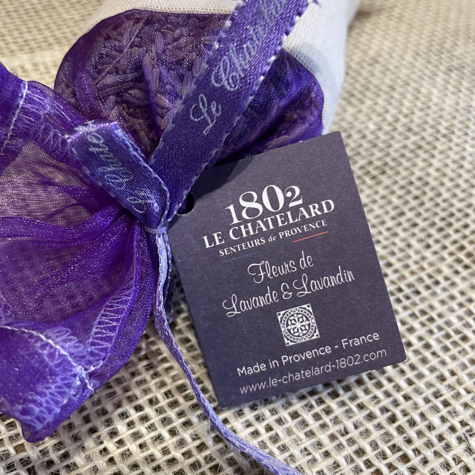 Purple sachet tied with ribbon and a product tag on burlap fabric