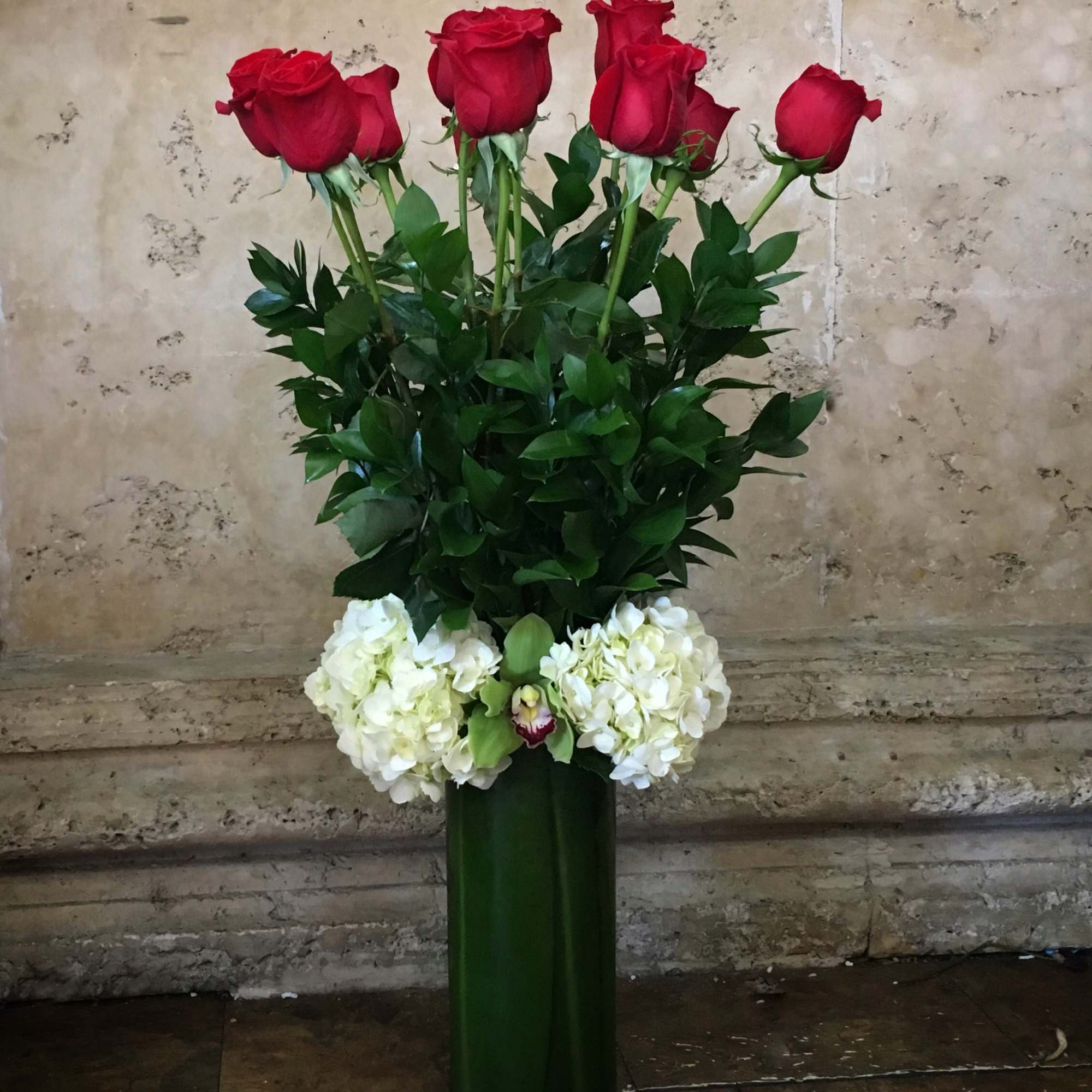 Tall vase arrangement of red roses with white hydrangeas