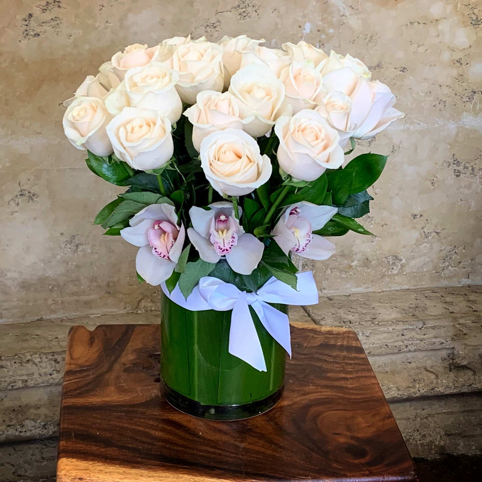 Cream roses and pale orchids in a green vase with a white ribbon