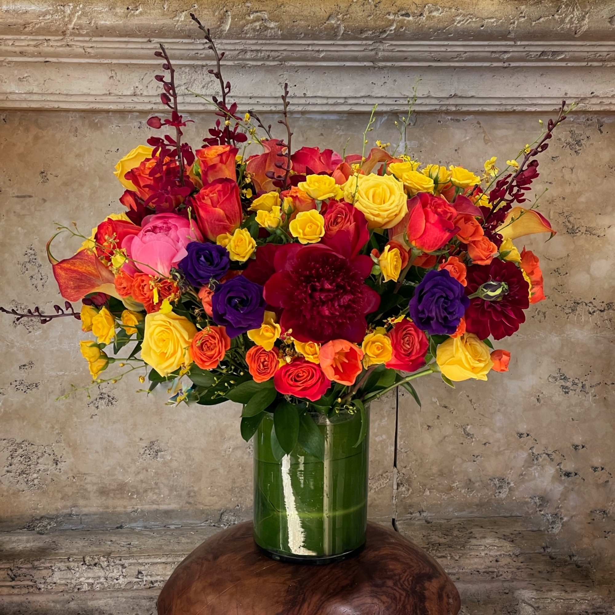 Colorful bouquet of roses and orchids in a green glass vase