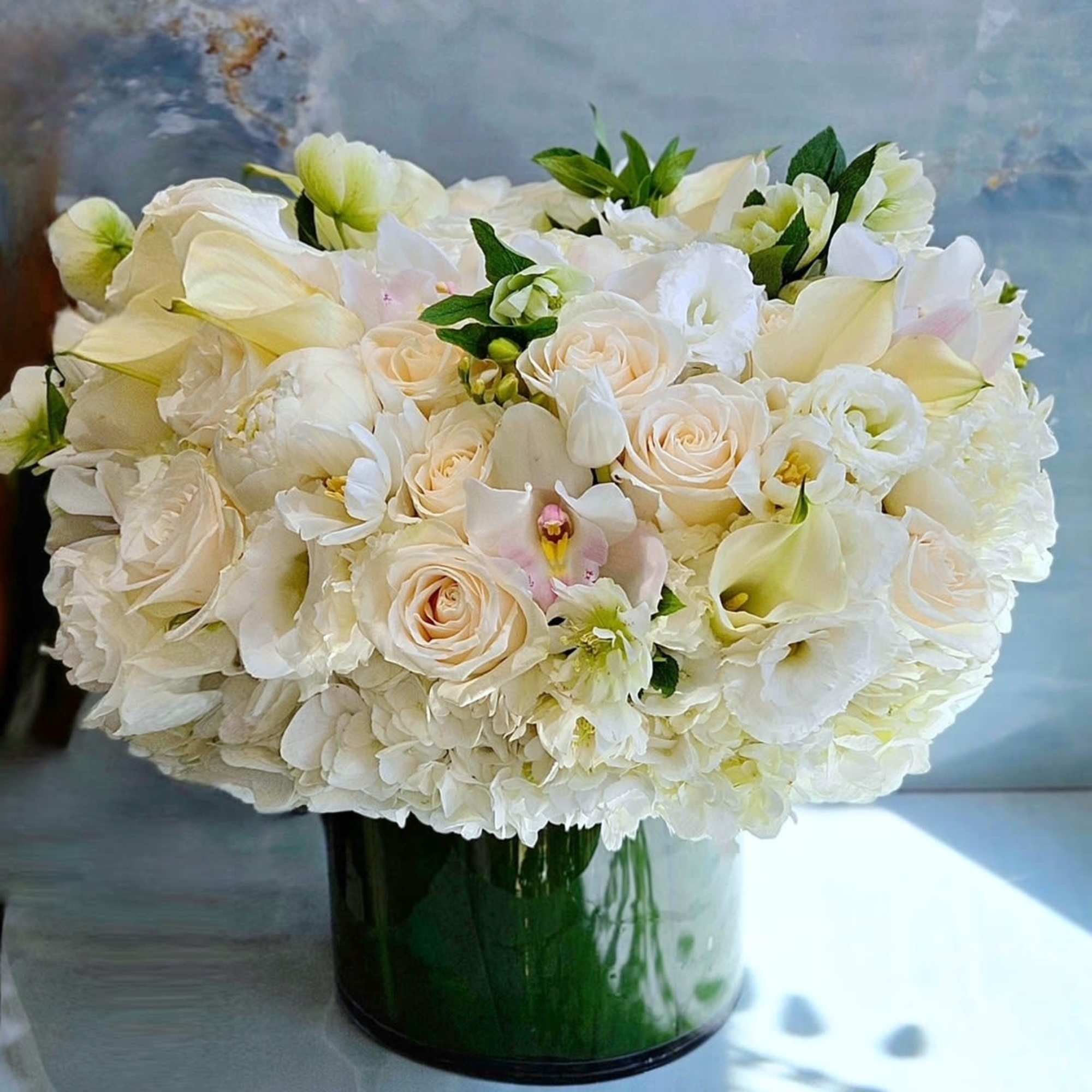 White floral arrangement in a green glass vase with roses and calla lilies