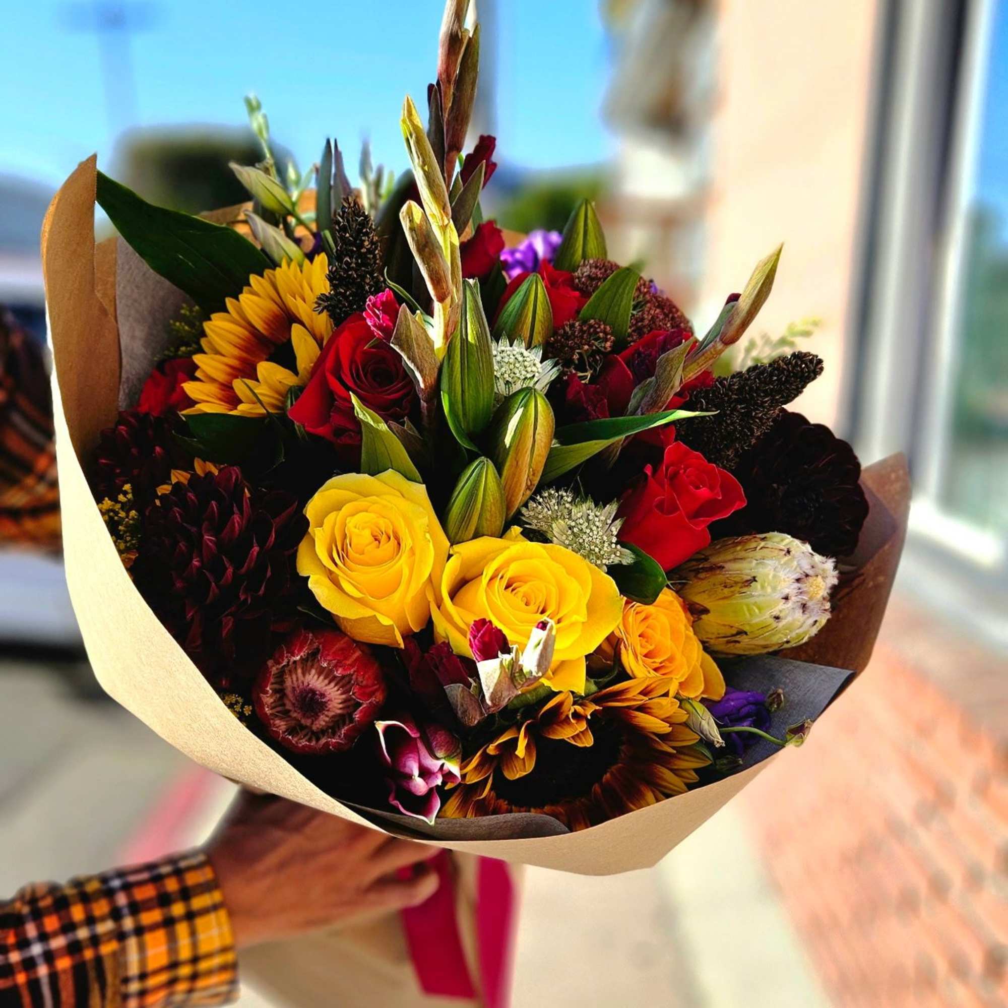 Mixed bouquet of roses, sunflowers, and protea wrapped in paper
