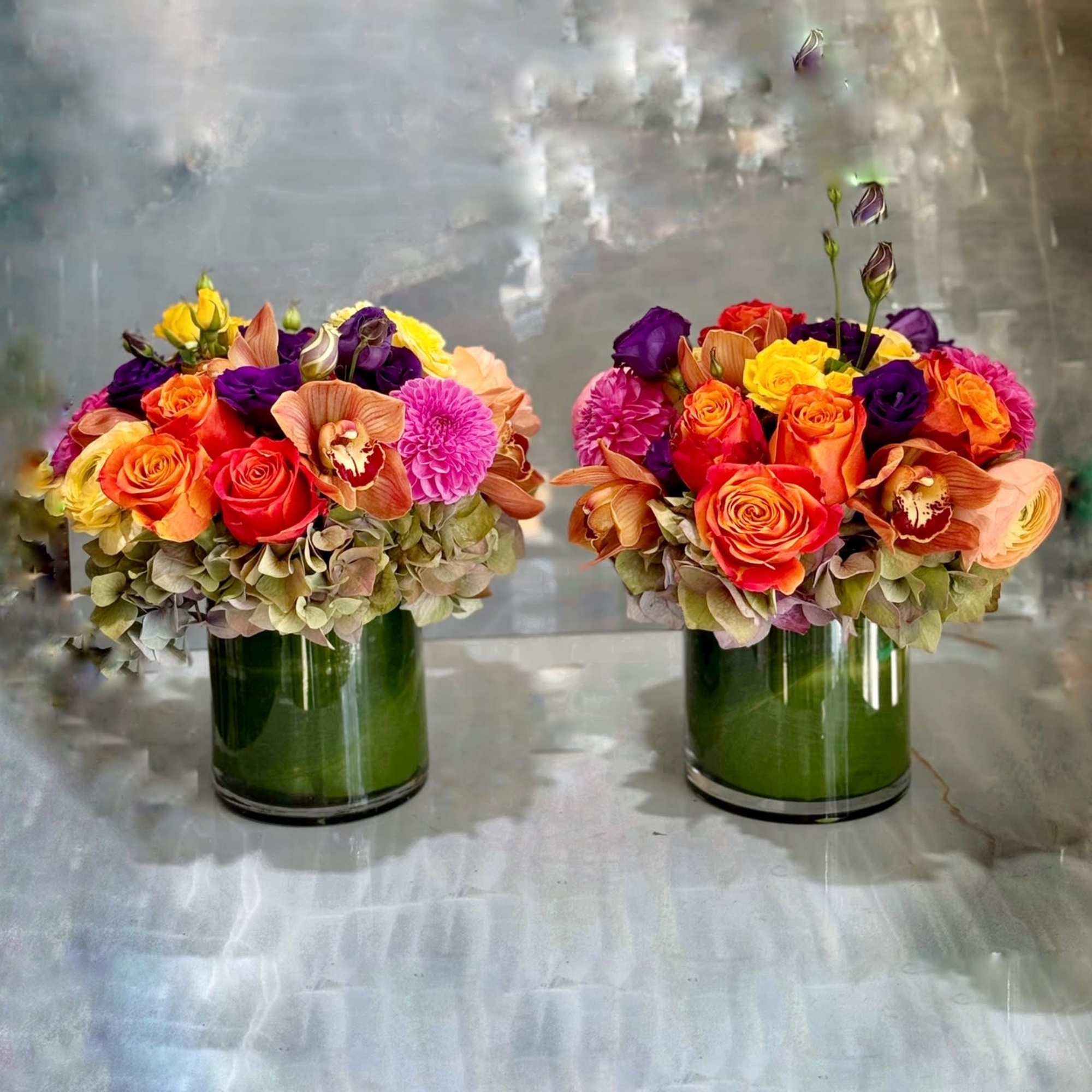 Two colorful flower arrangements in green glass vases