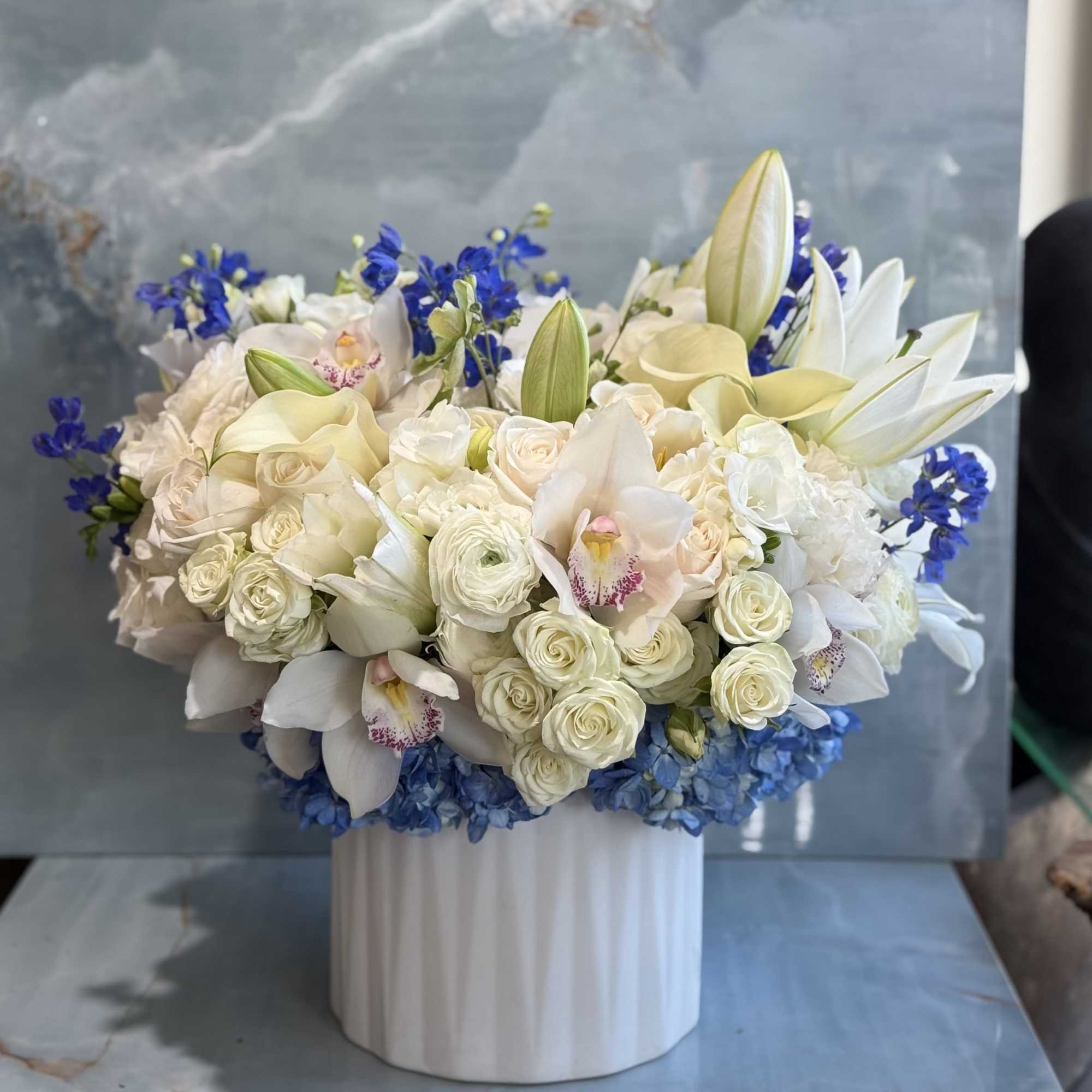 White roses, lilies, orchids, and blue flowers in a white vase