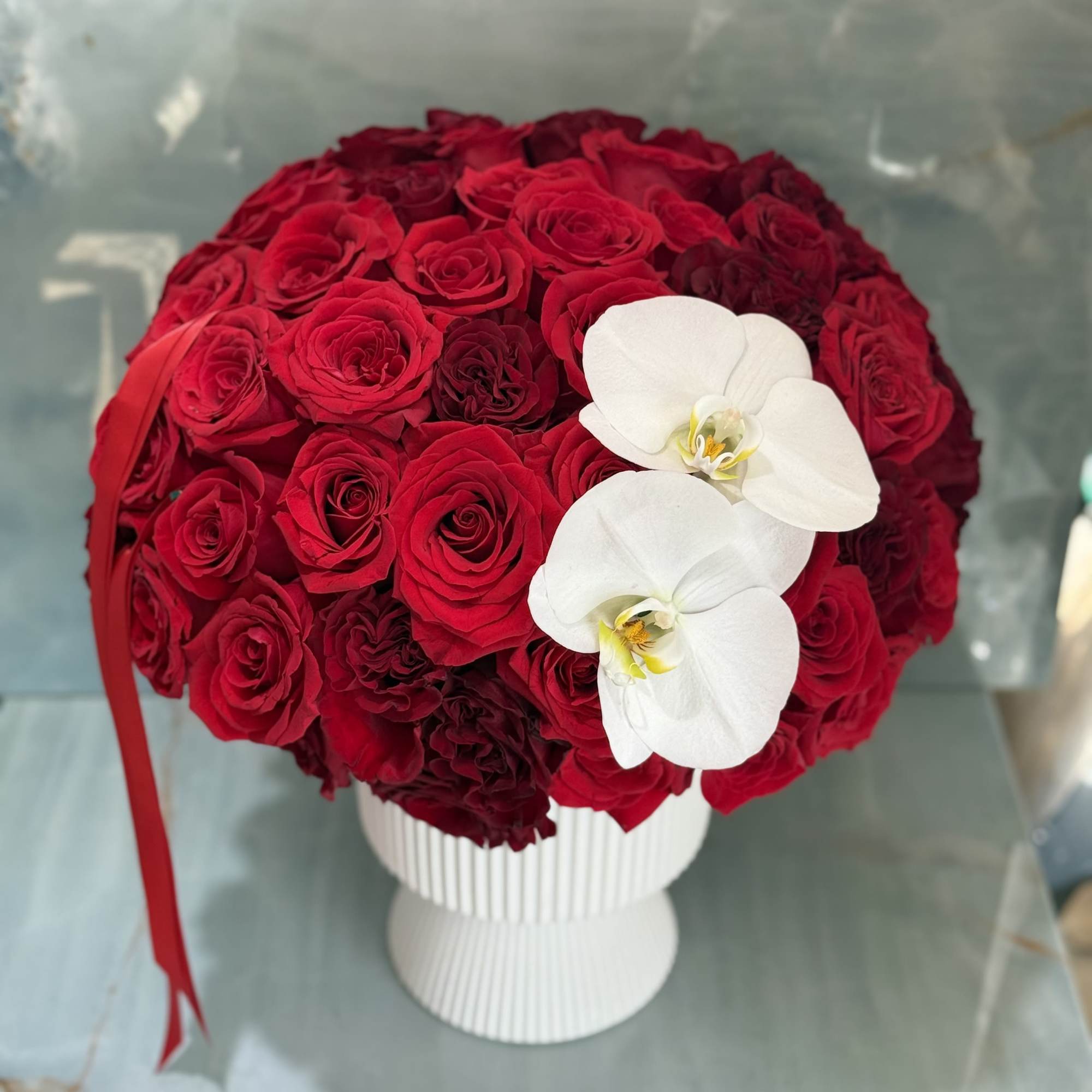 Round bouquet of red roses with two white orchids in a white vase