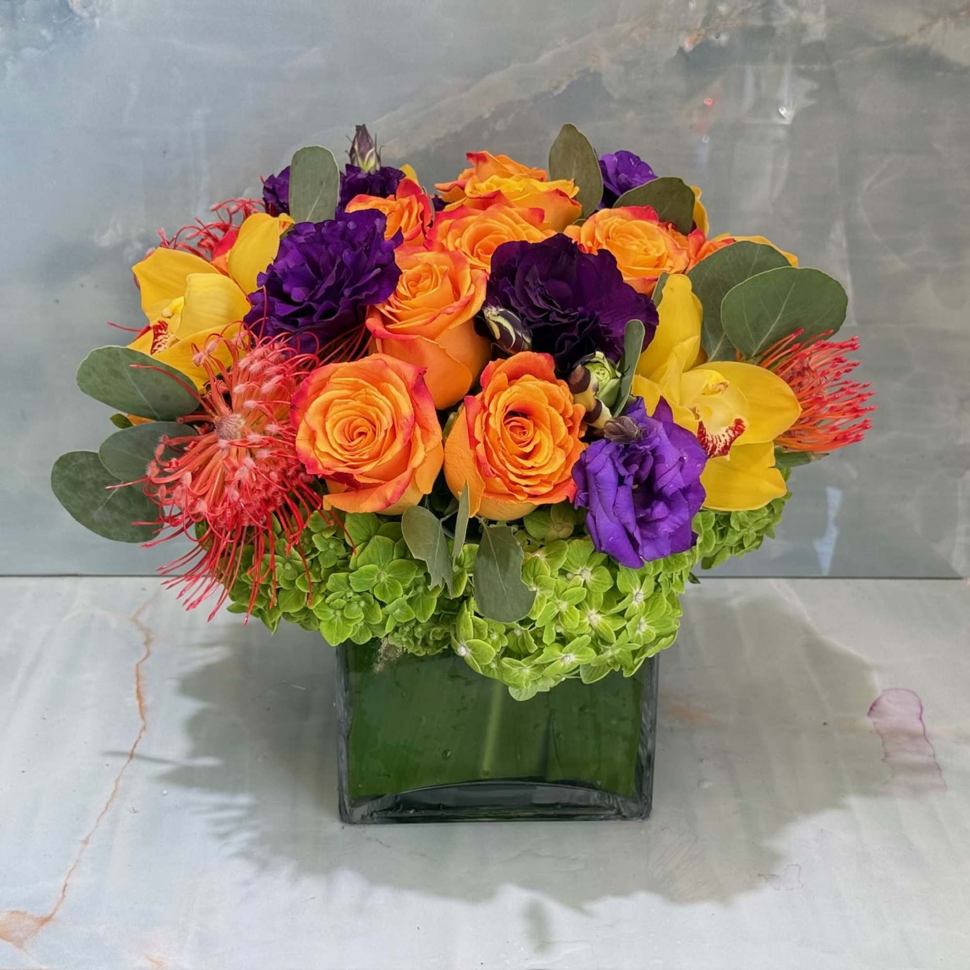 Colorful bouquet of roses, orchids, and hydrangeas in a green glass vase