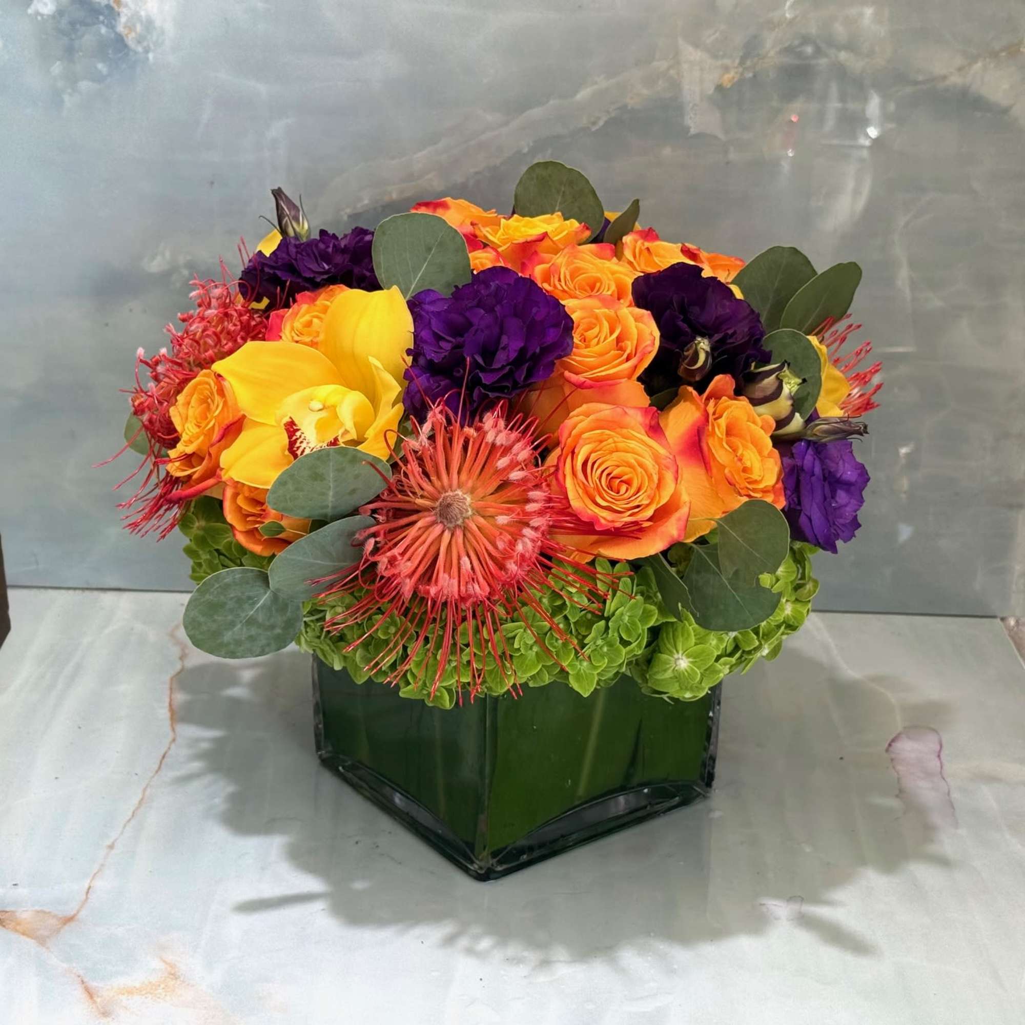 Orange and purple roses in a square glass vase with green hydrangeas