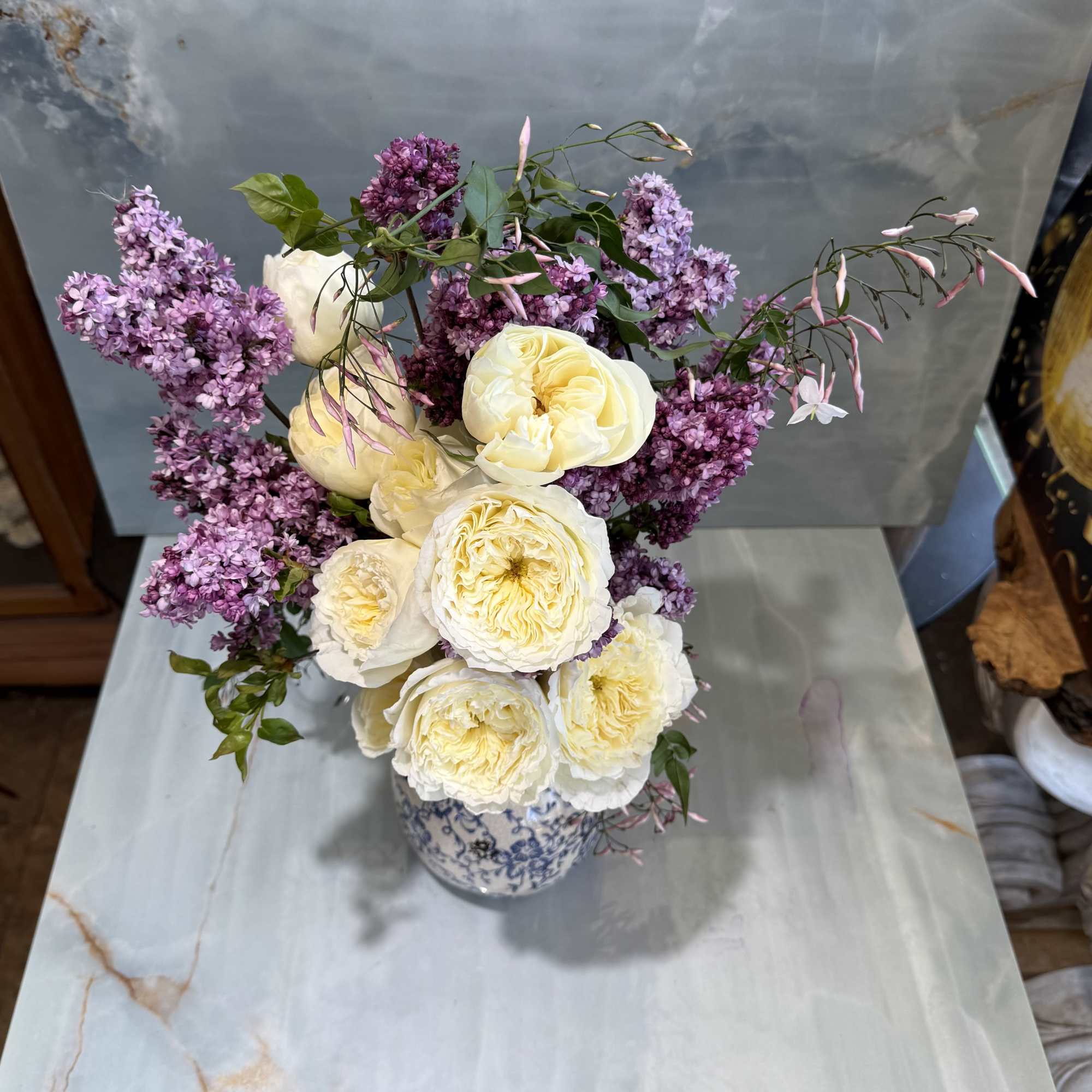 Cream roses and purple lilacs arranged in a blue-and-white vase.