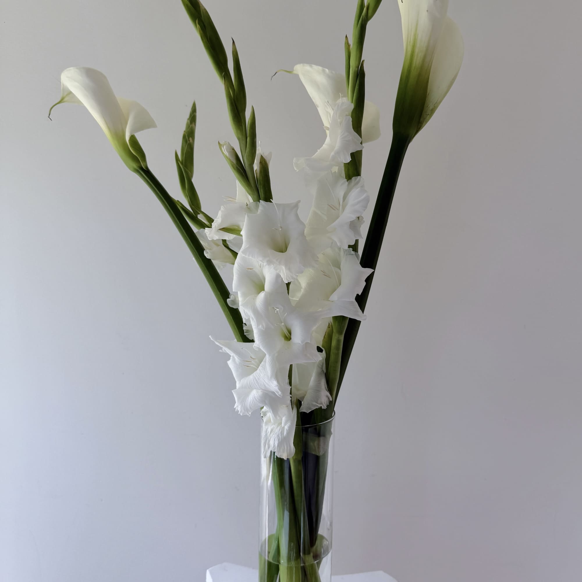 This floral design features white calla lilies and white gladiolus, two blooms