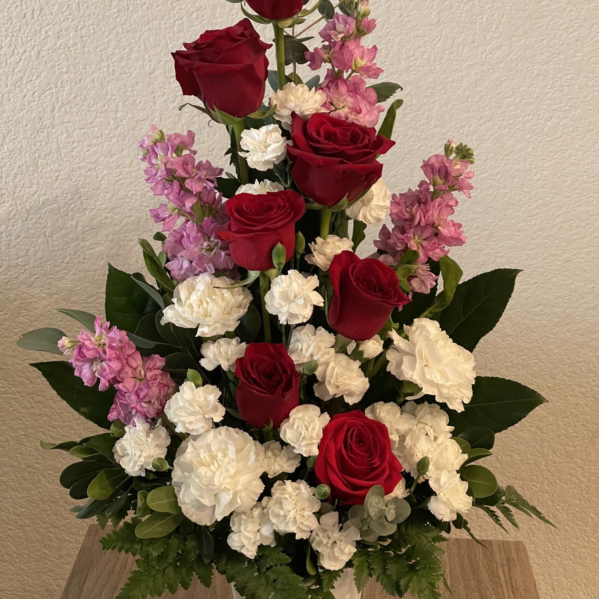 Deep, velvety red roses rise through clusters of soft white carnations and