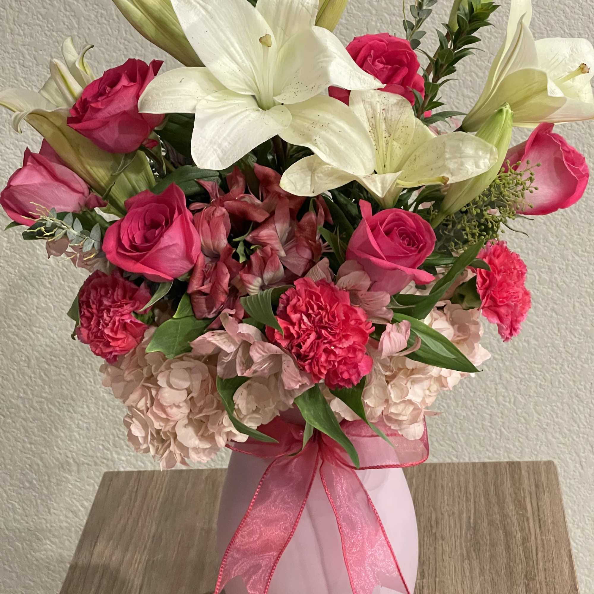 Bright white lilies rise above vivid hot-pink roses and carnations in this