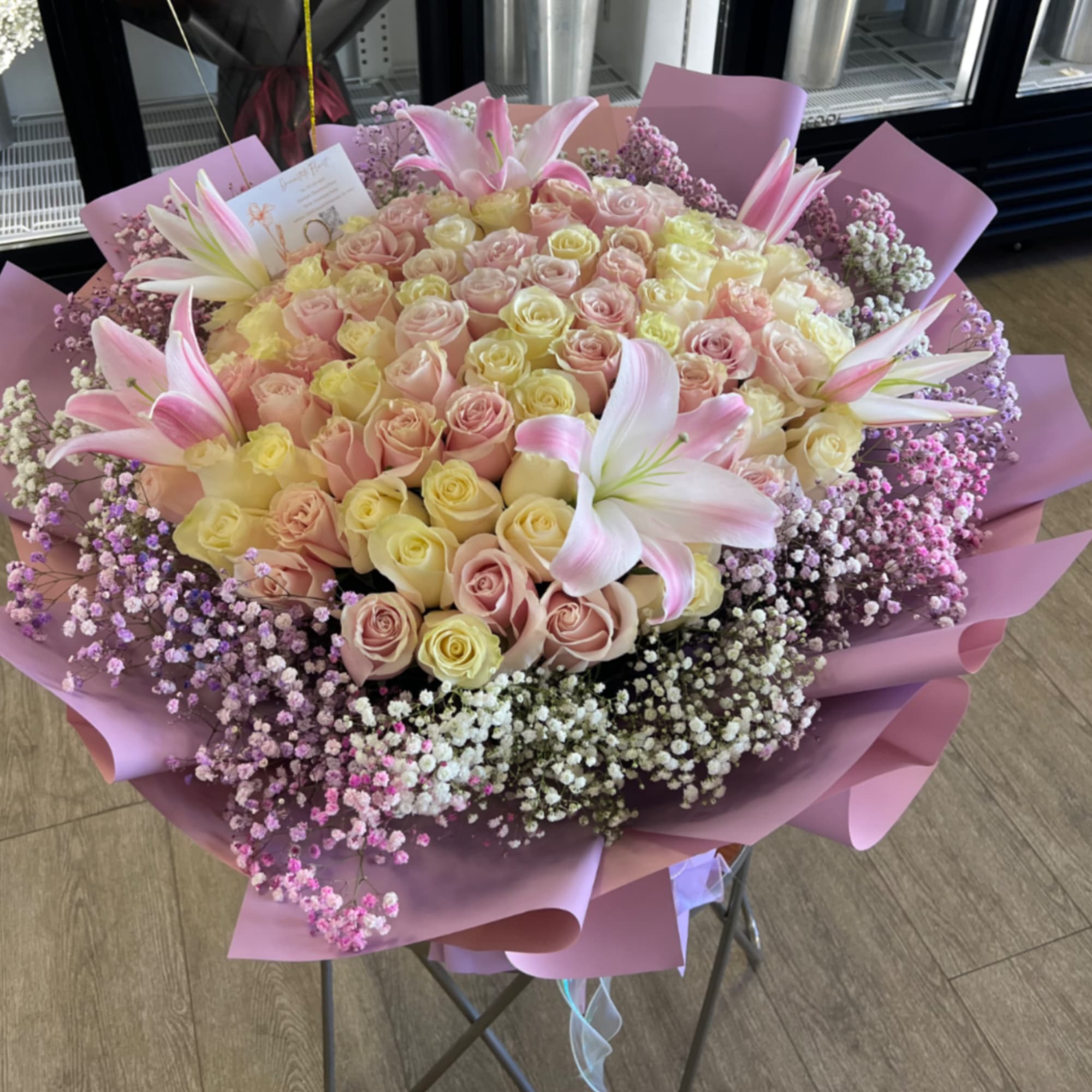 Pale pink and white roses with pink-and-white lilies, framed by purple and
