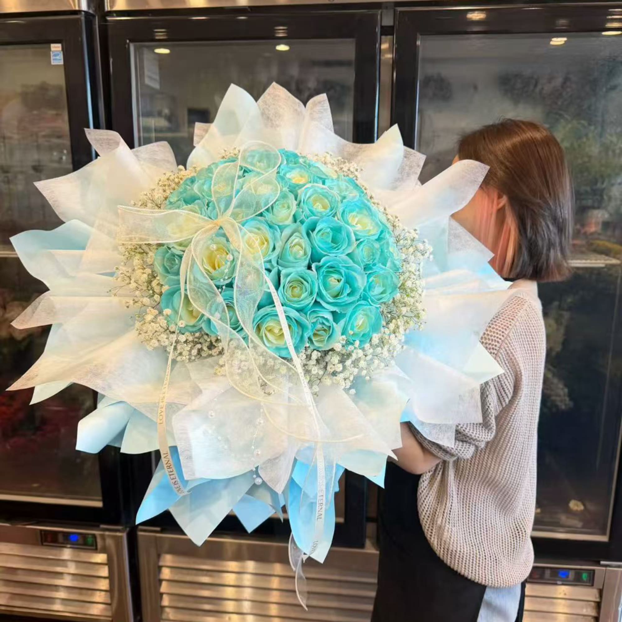 Large turquoise rose bouquet wrapped in white paper with a ribbon