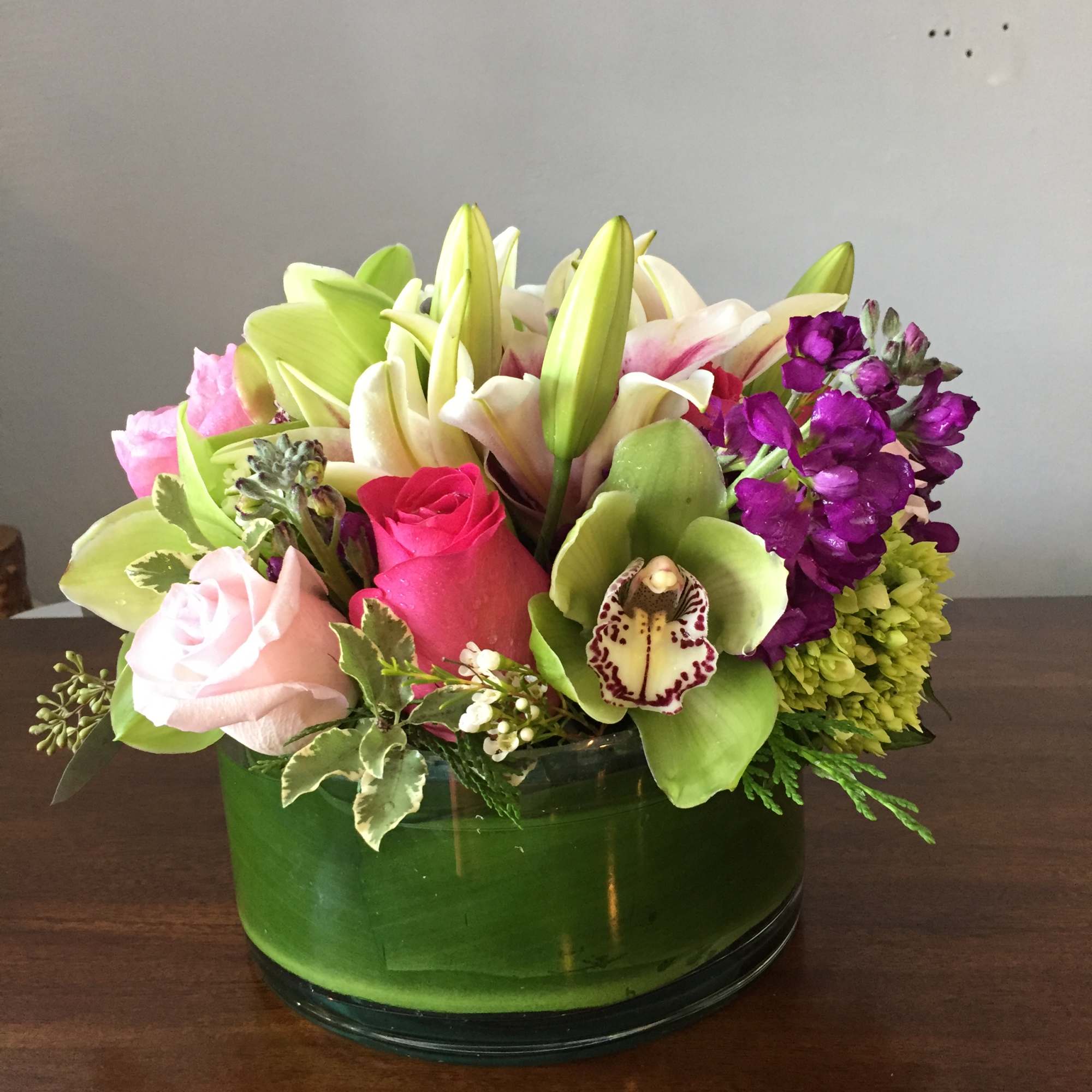 Mixed bouquet in a green glass vase with lilies, roses, orchids, and hydrangea