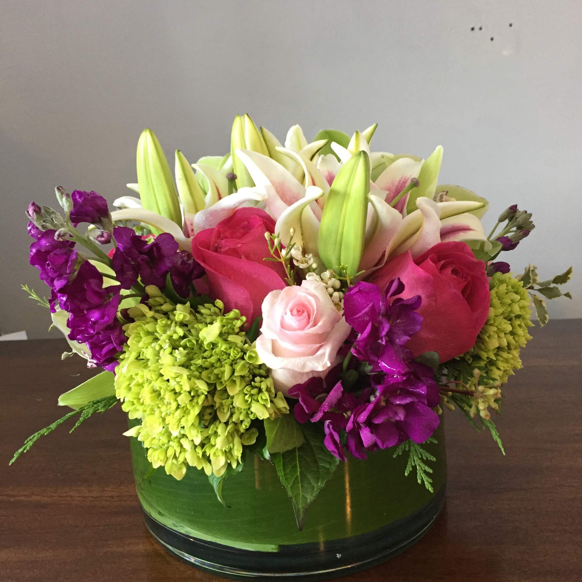 Mixed bouquet with lilies, roses, and purple blooms in a glass bowl vase