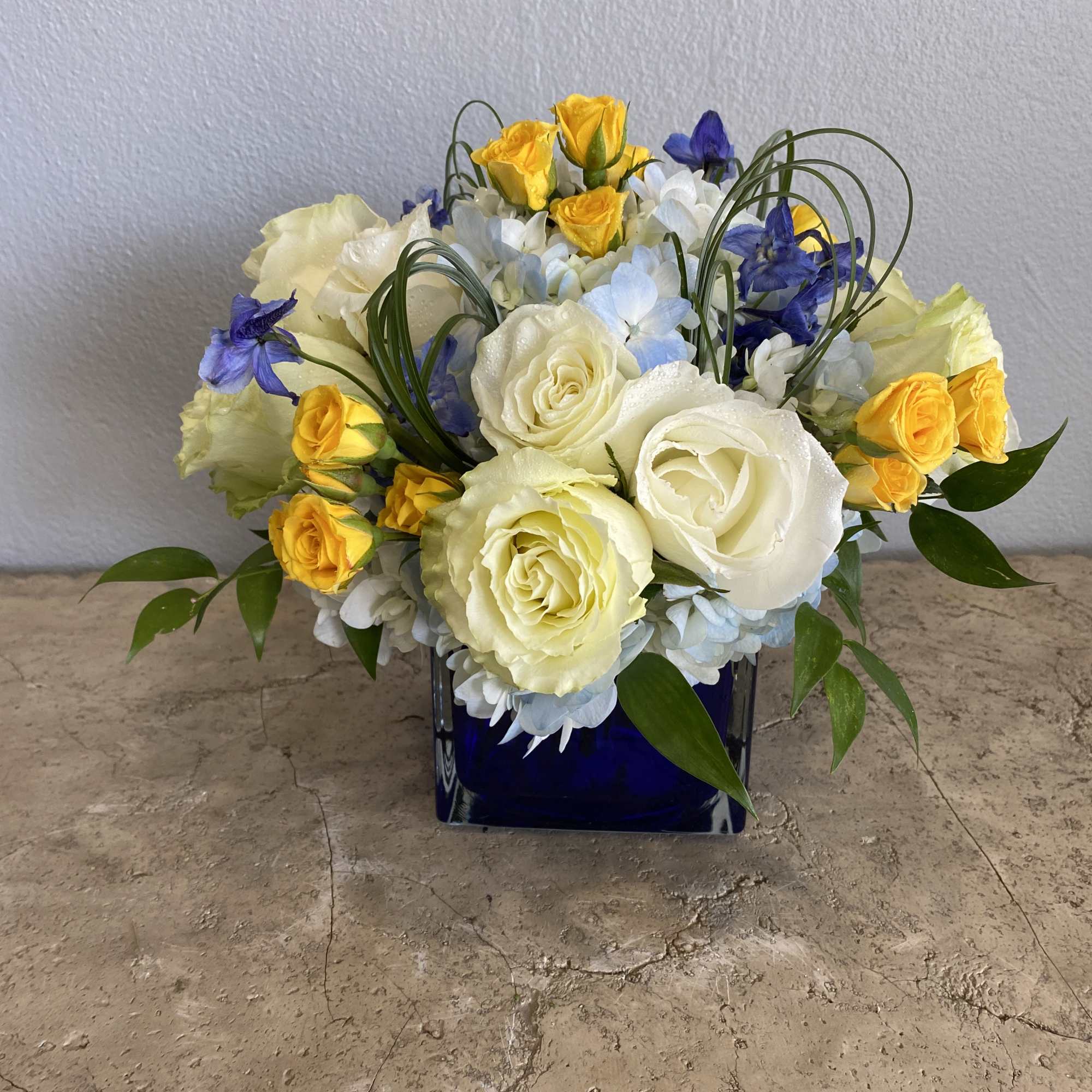 White and yellow rose arrangement in a blue glass vase