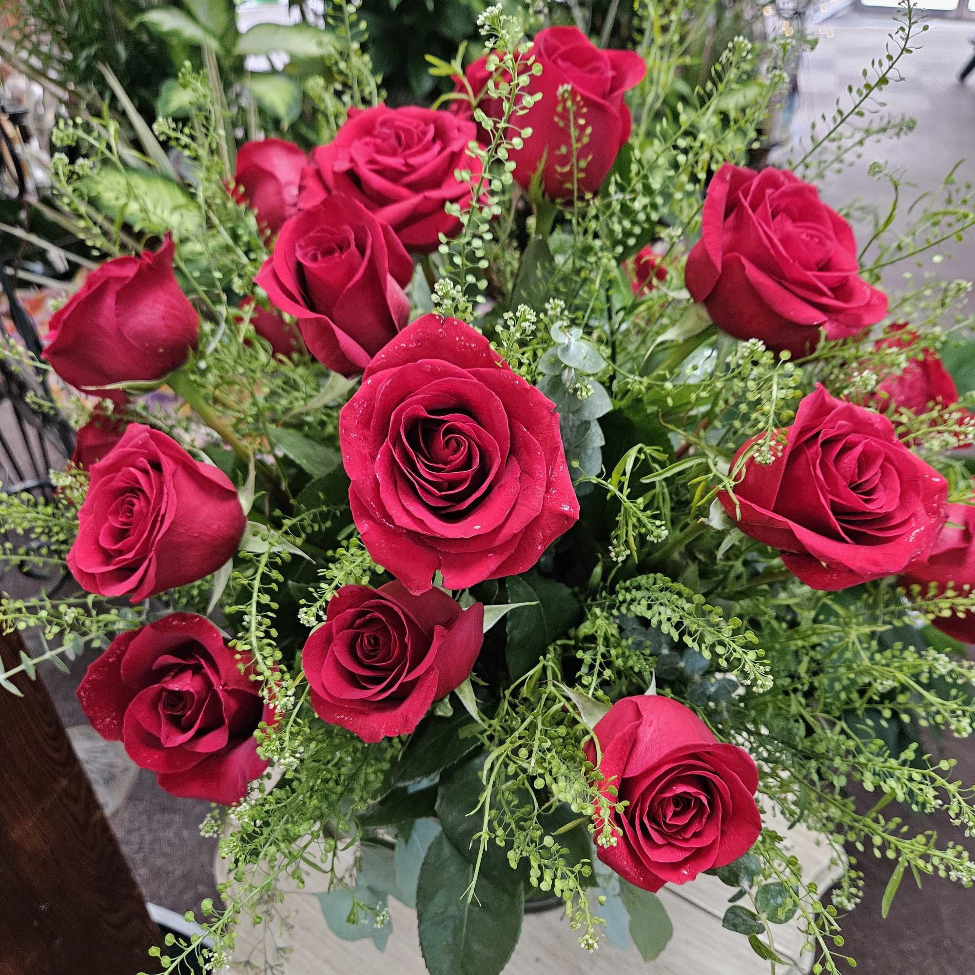 Arrangement of red roses with airy green filler in a vase on a small light wood table