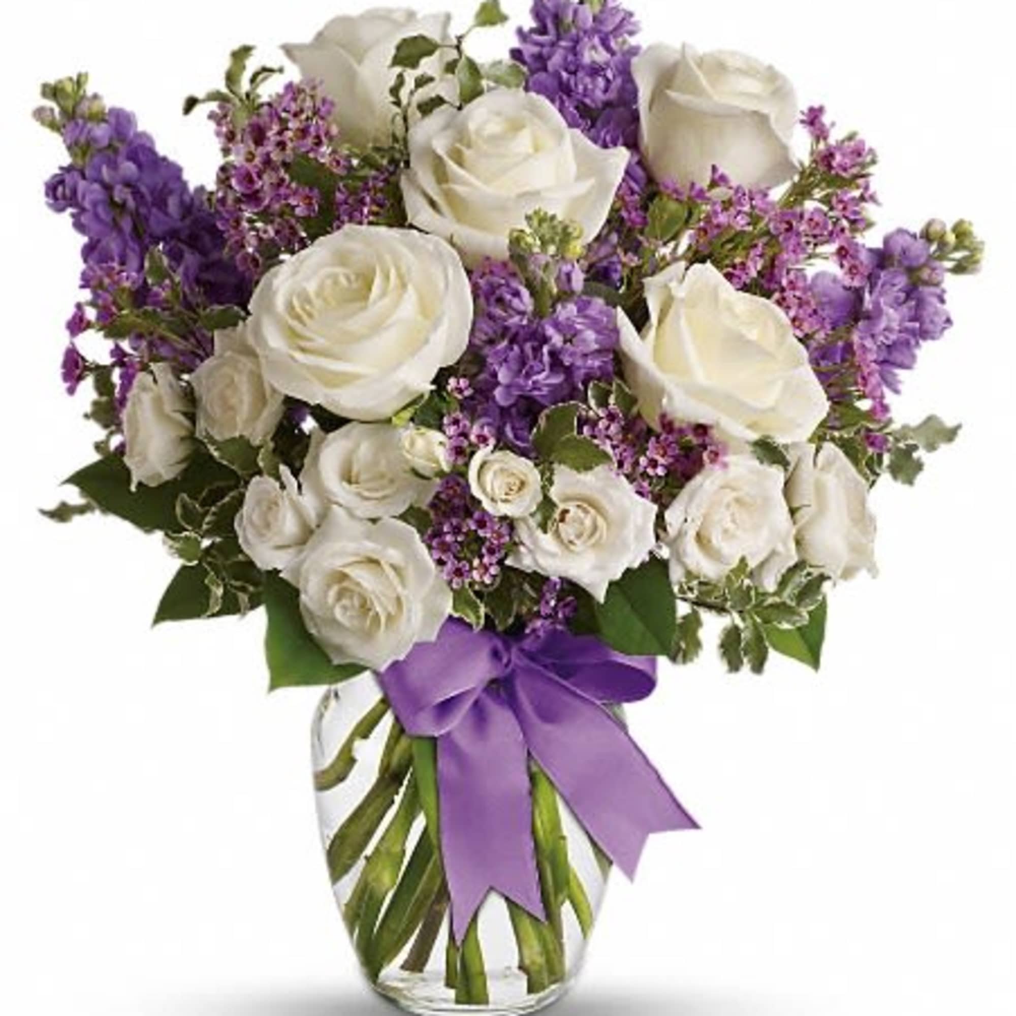 White roses and purple flowers arranged in a clear glass vase with a purple ribbon