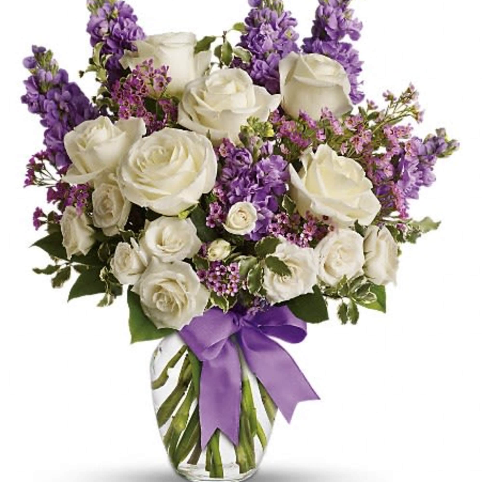 White roses and purple flowers arranged in a glass vase with a purple ribbon