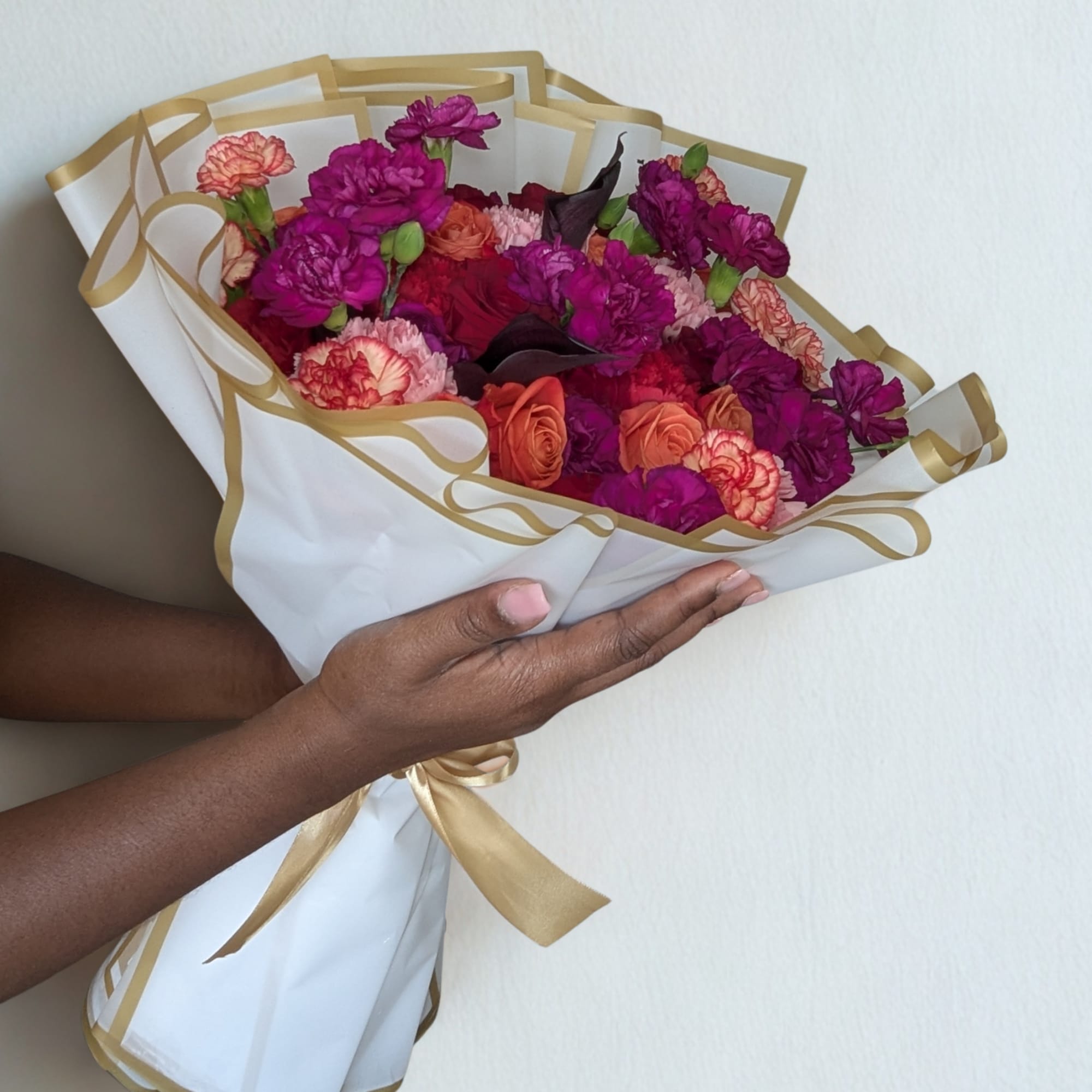 Handheld bouquet of pink, purple, and coral flowers wrapped in white paper