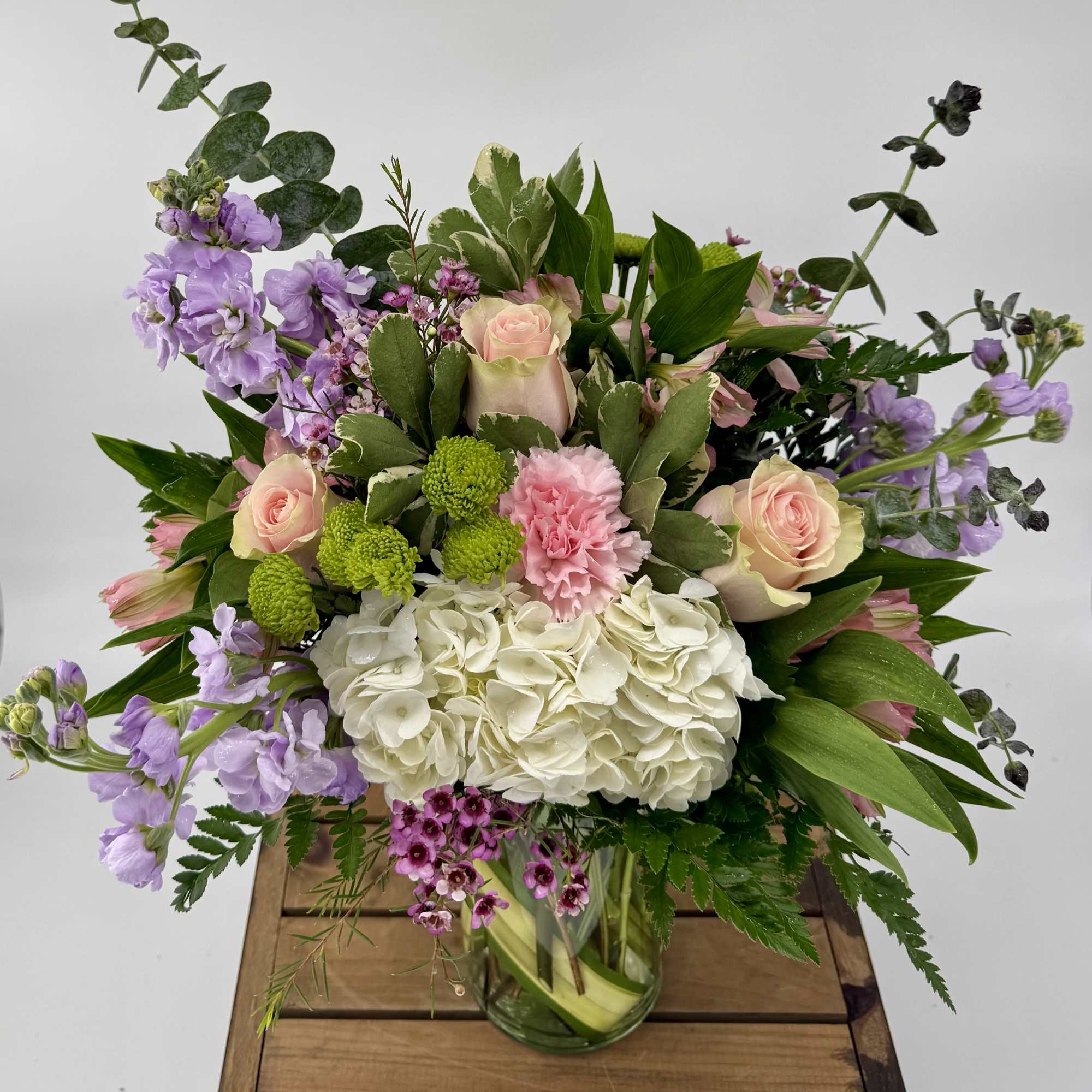 Pastel arrangement of pink roses, carnations, lavender stock and white hydrangea in a glass vase