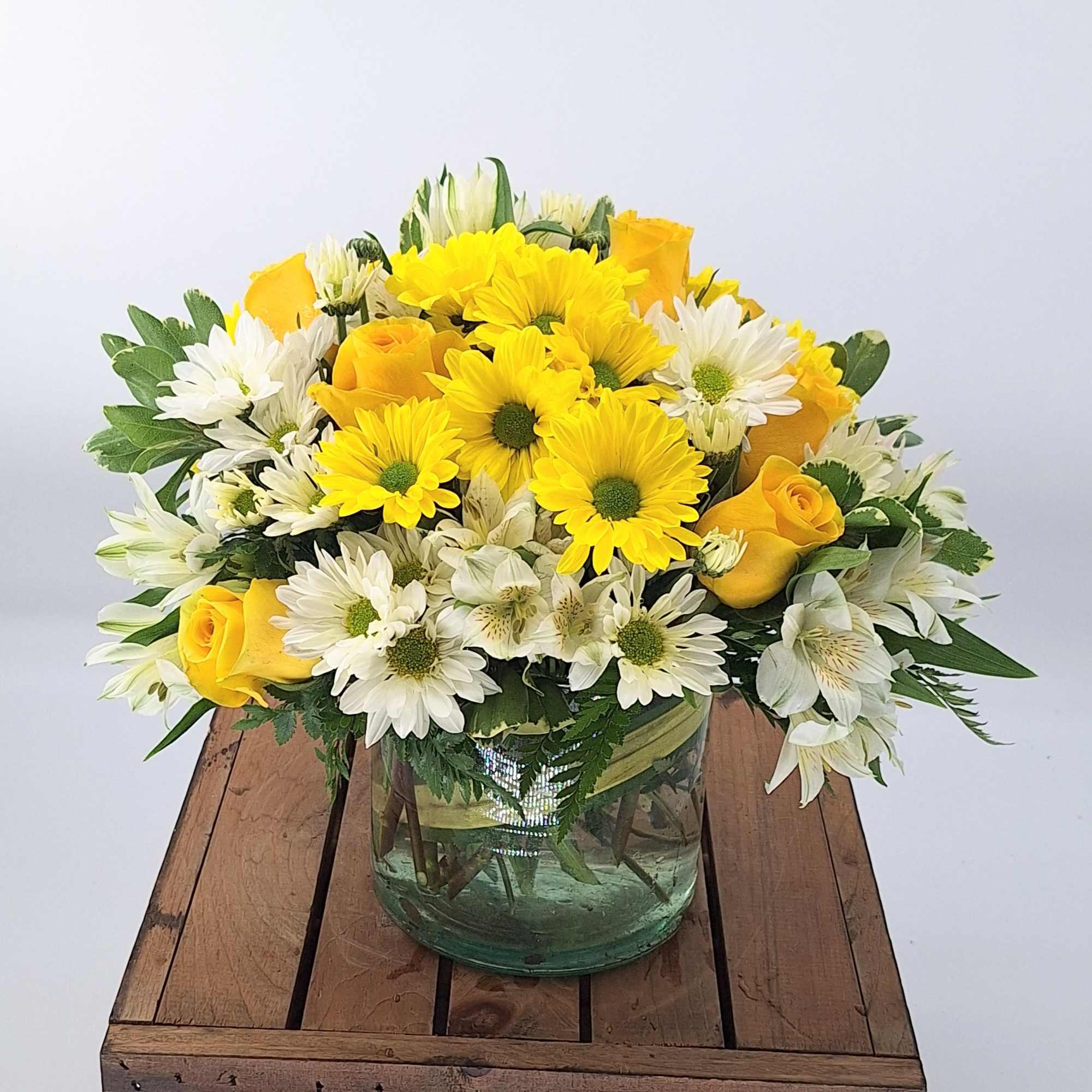 Low arrangement of yellow roses and daisies with white daisies and alstroemeria in a clear glass vase
