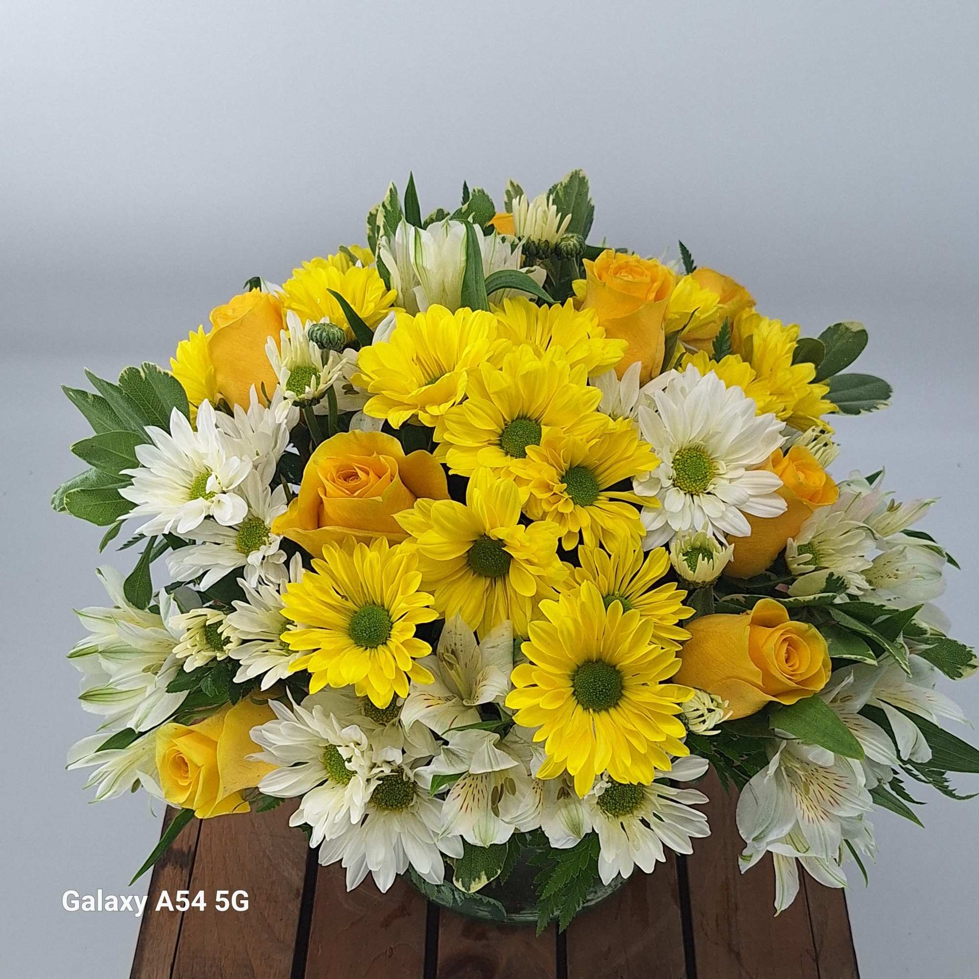 Low round bouquet of yellow roses and yellow and white daisies in a clear glass vase
