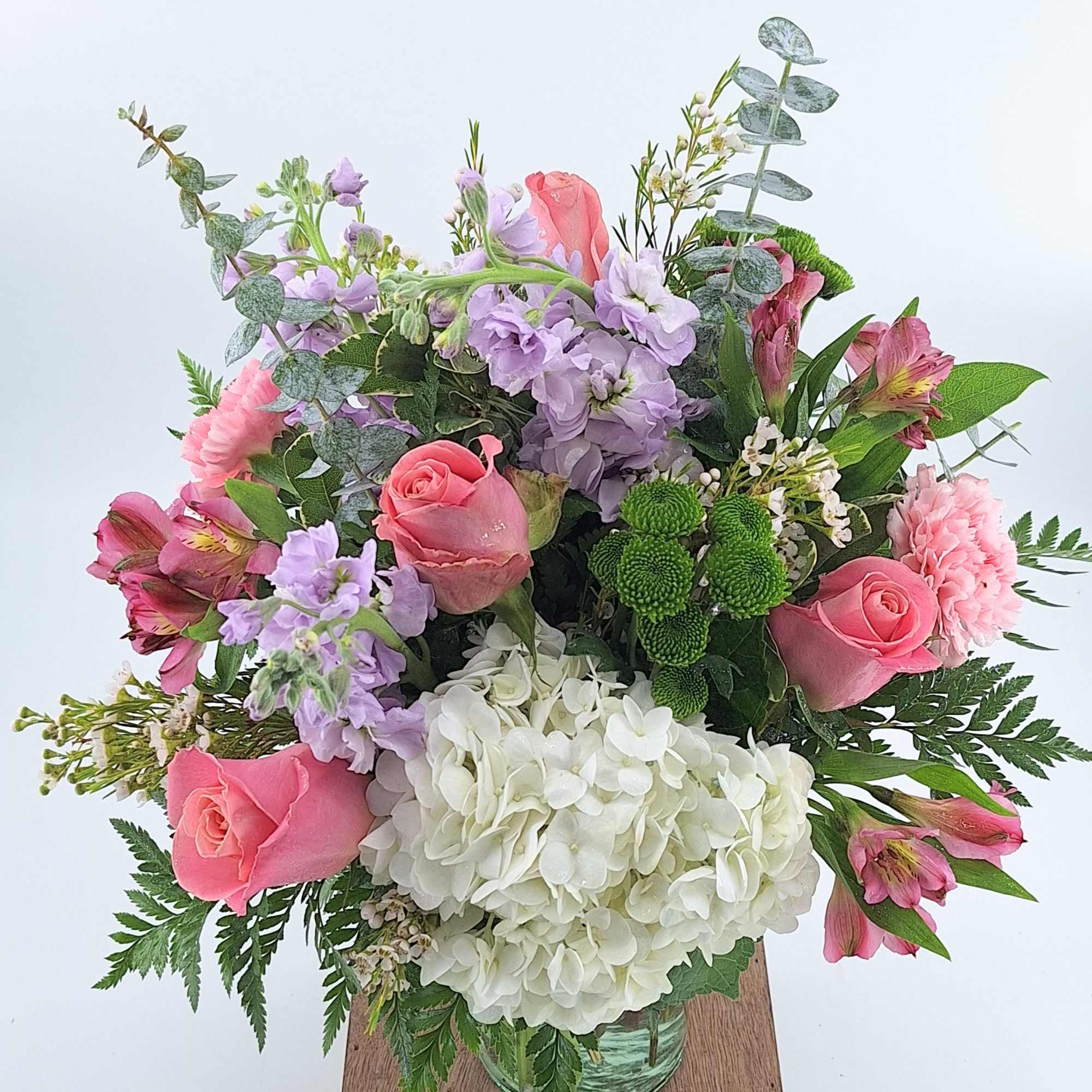 Mixed bouquet of pink roses, lavender blooms, and white hydrangea in a clear glass vase