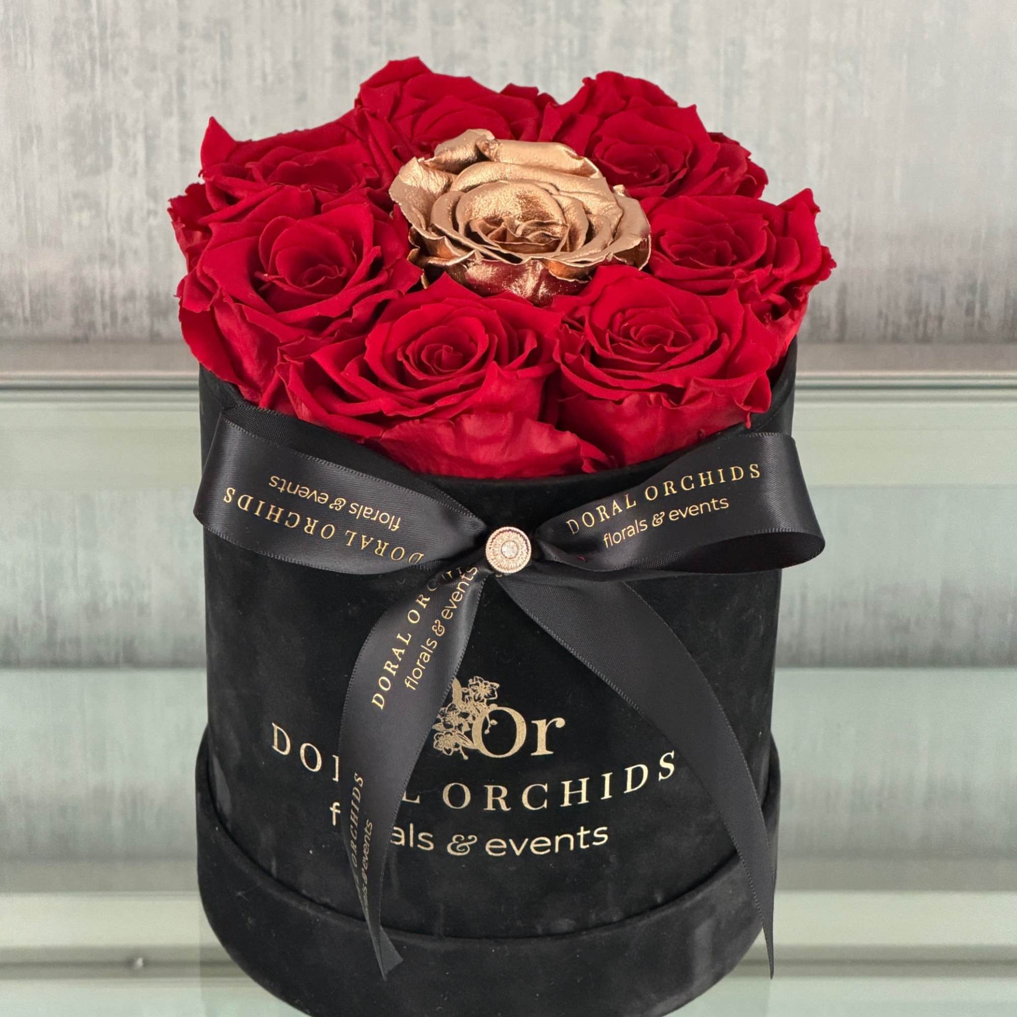 Red roses and a gold rose in a black hatbox with a ribbon