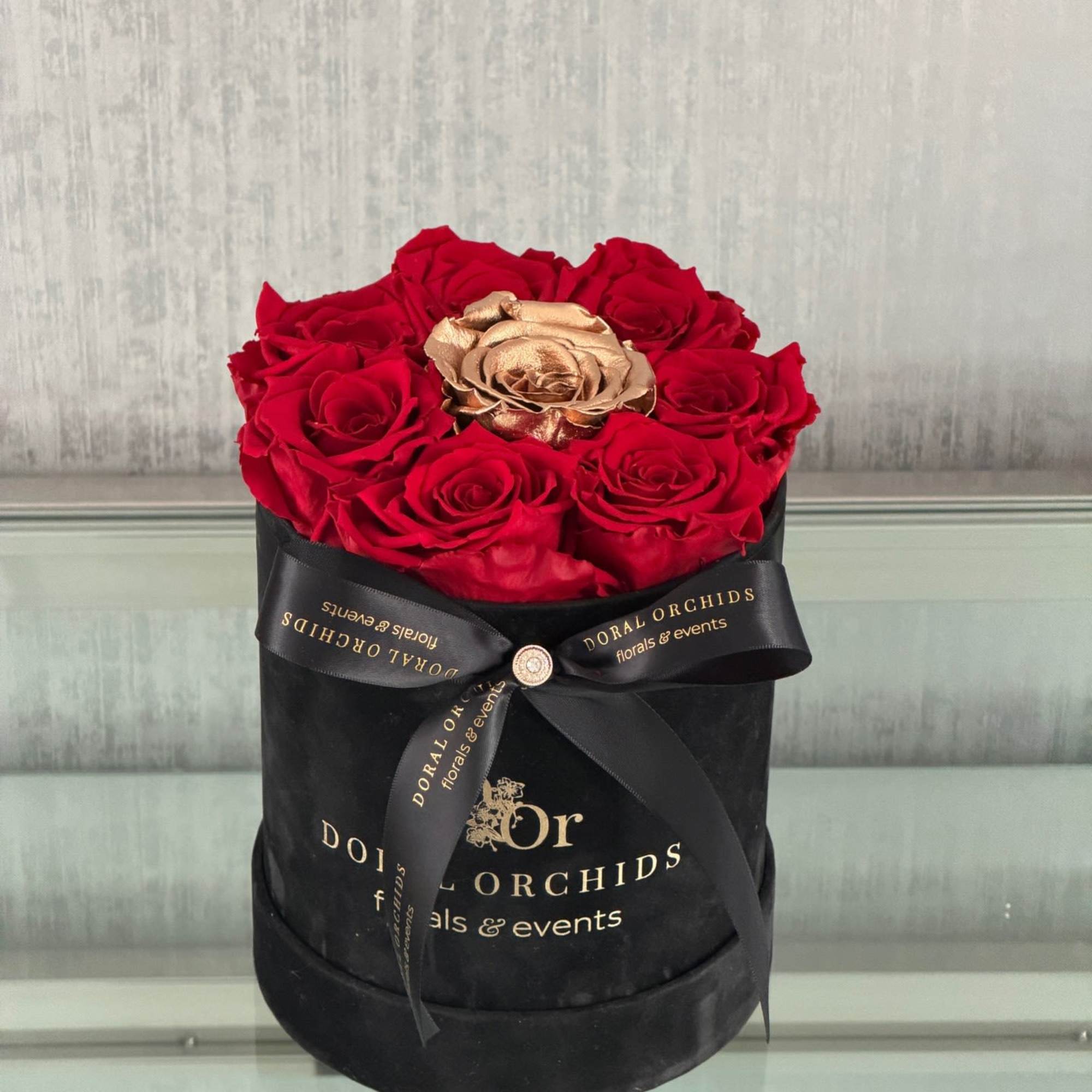Red roses in a black round box with a gold rose in the center