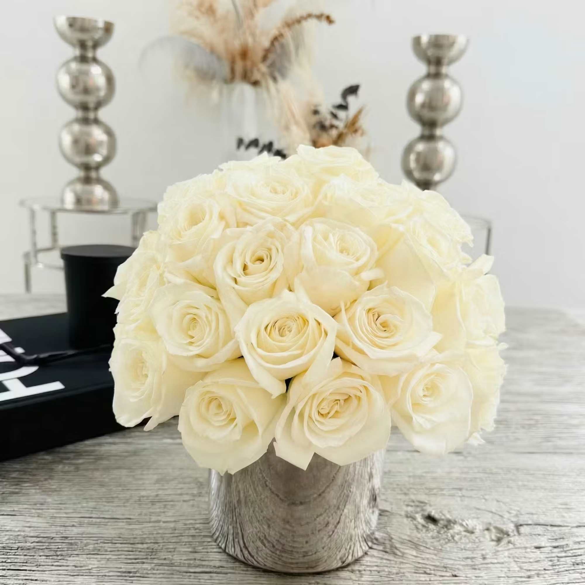 Compact arrangement of ivory roses in a silver vase on a light wood table