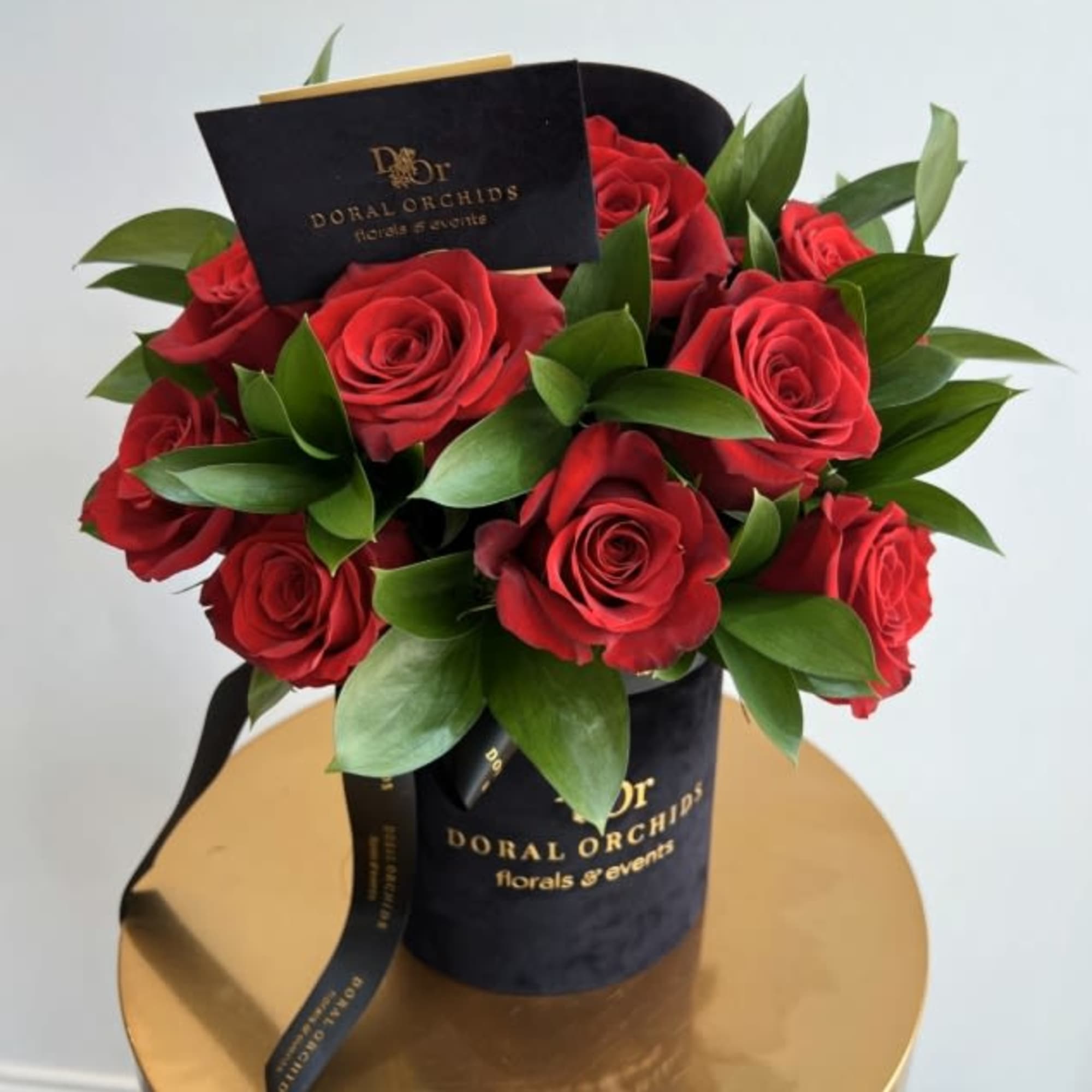 Hatbox arrangement of red roses in a black round container with gold lettering and a card.