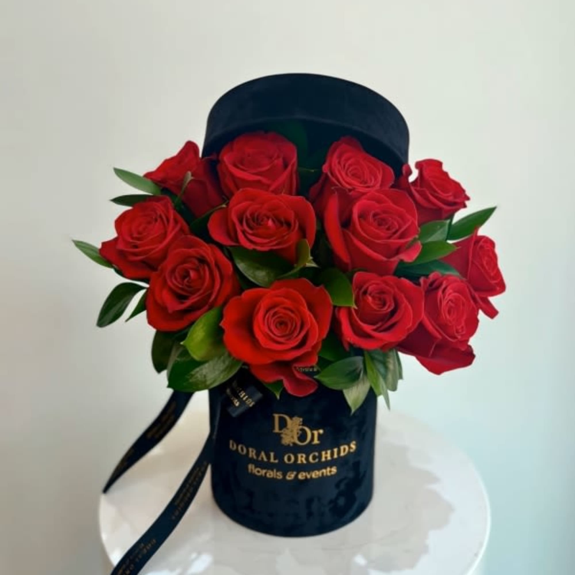 Hatbox arrangement of red roses in a black velvet cylinder container with gold lettering.