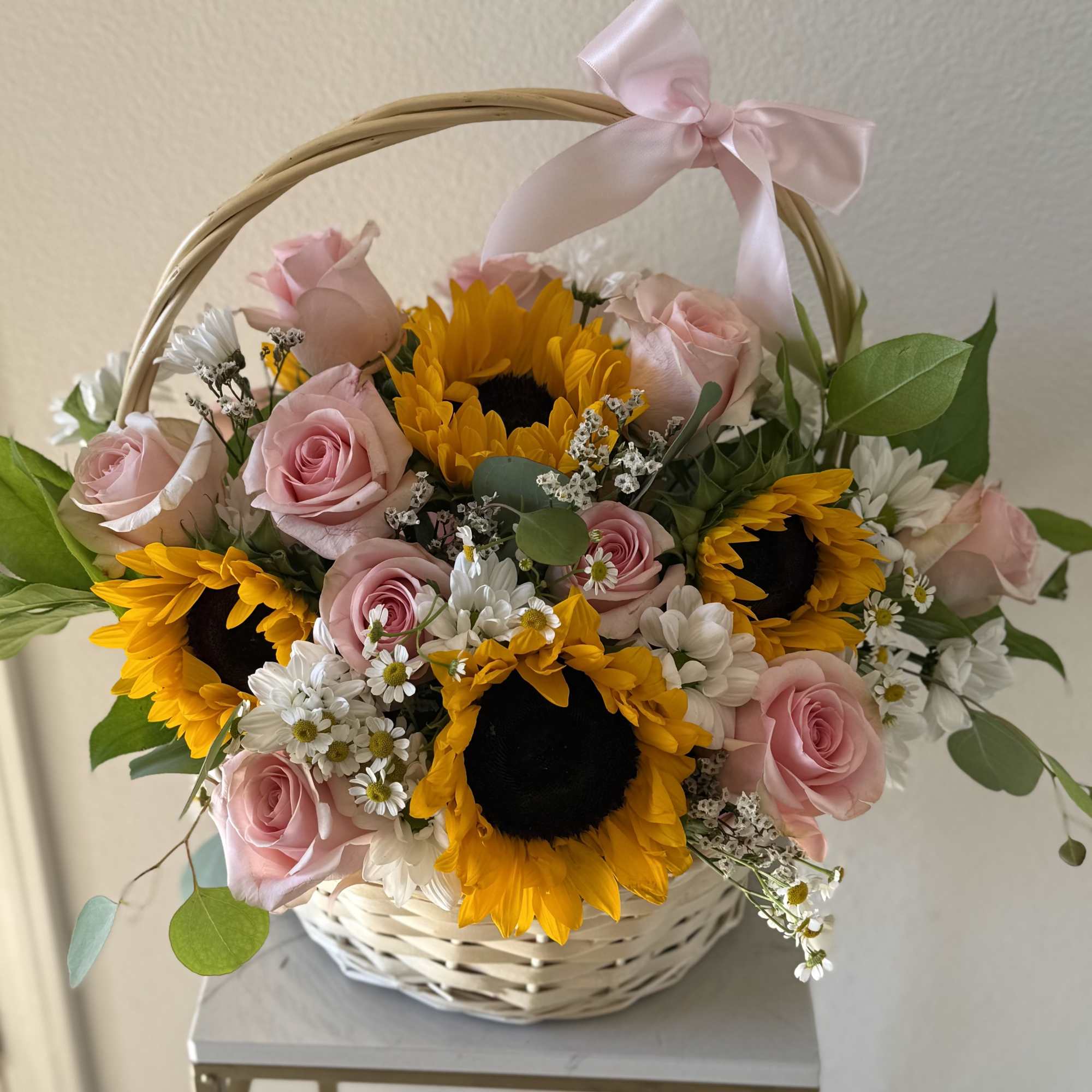 Basket arrangement of pink roses and sunflowers with a pink ribbon