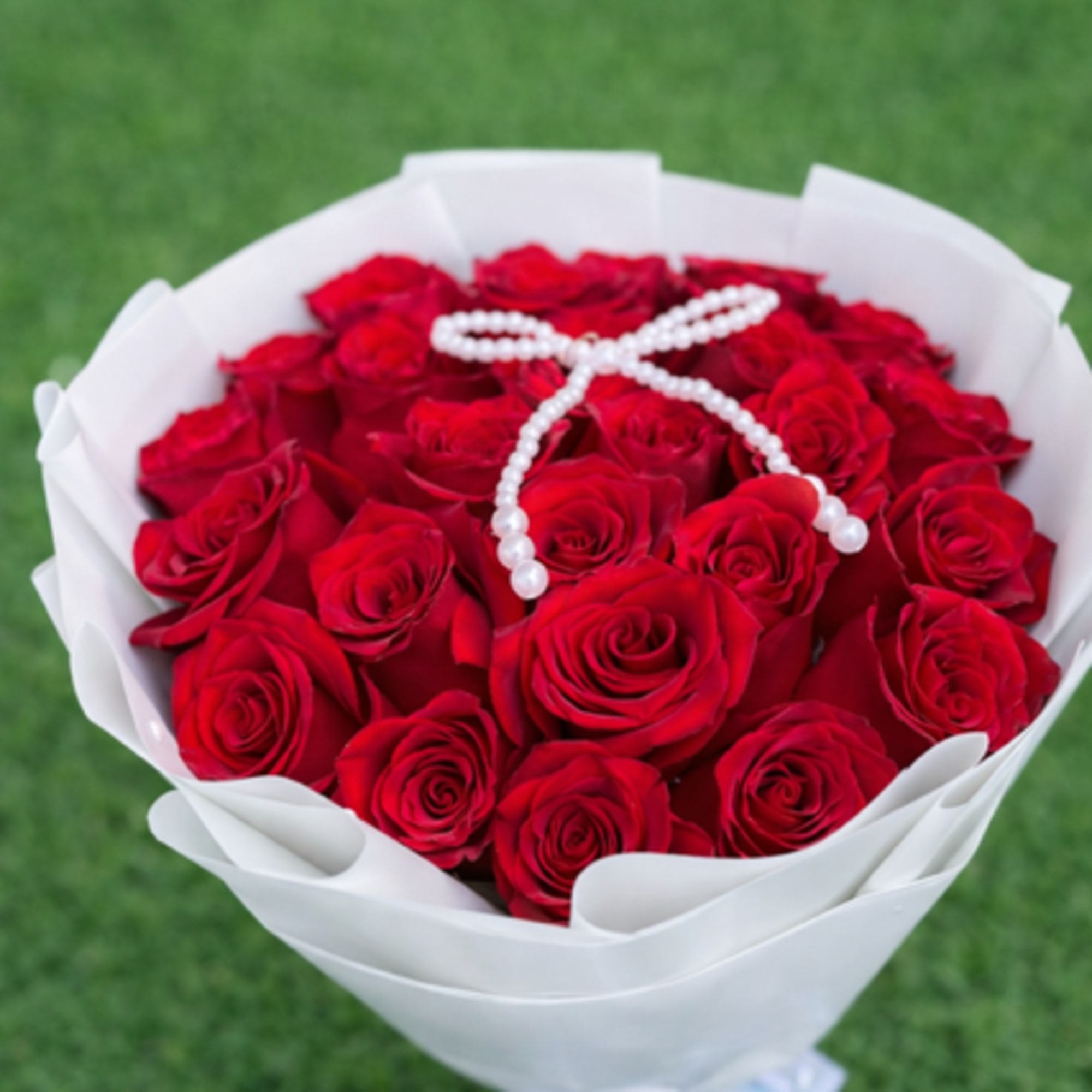 Bouquet of red roses wrapped in white paper with a pearl ribbon