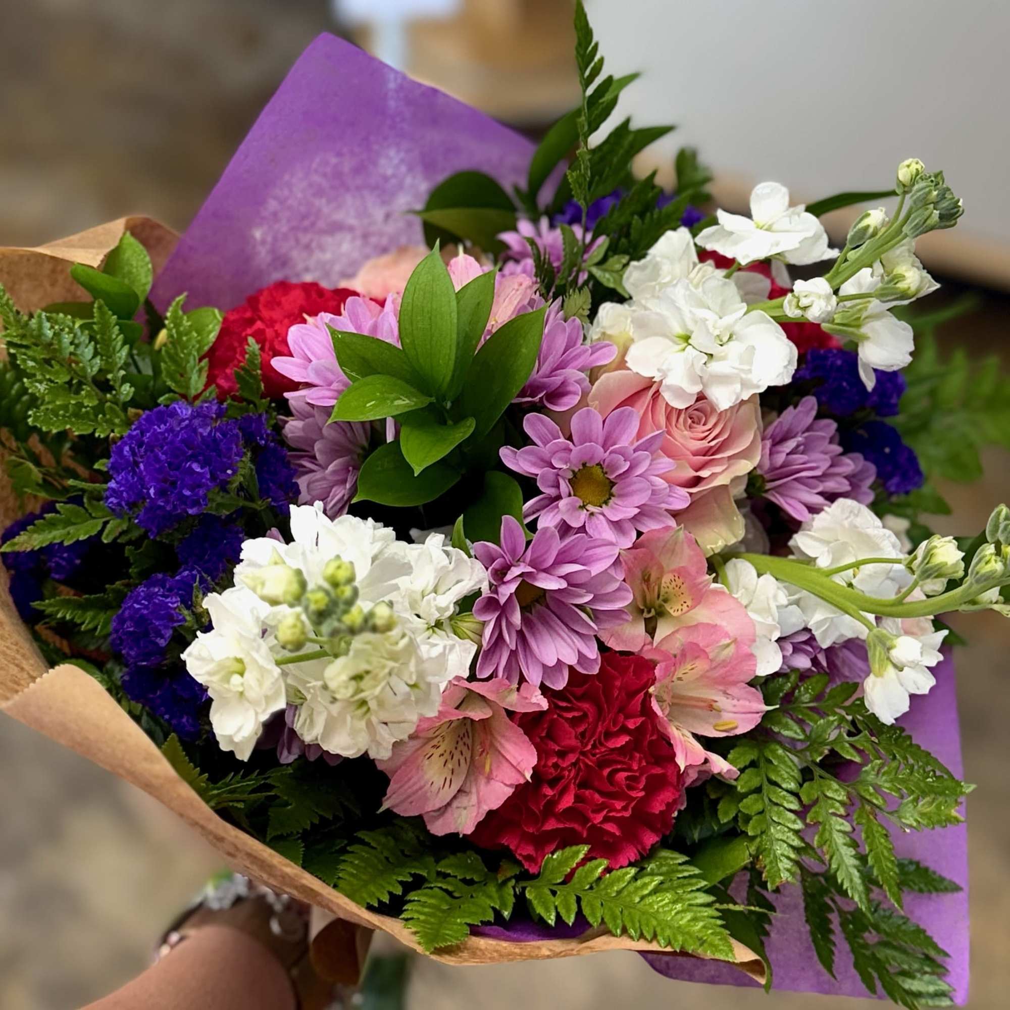 Mixed bouquet of pink, white, purple, and red flowers wrapped in brown and purple paper