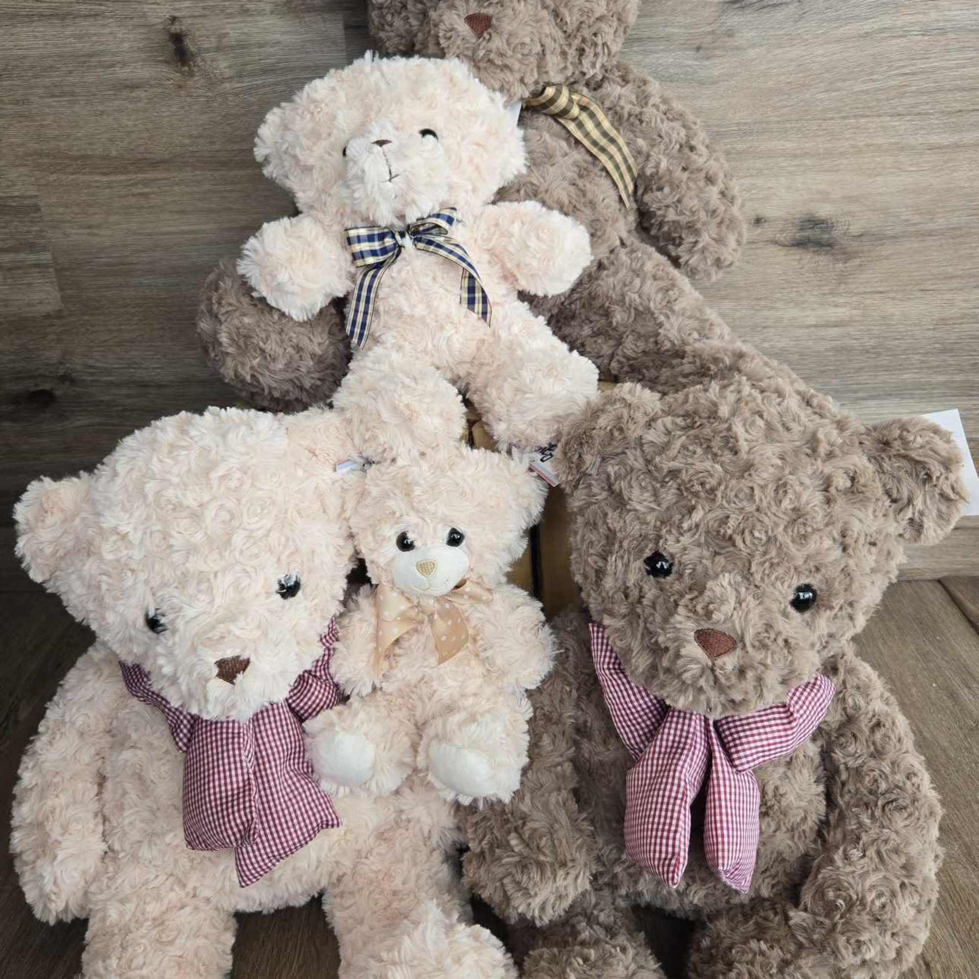 Four plush teddy bears with ribbon bows arranged on a wooden floor