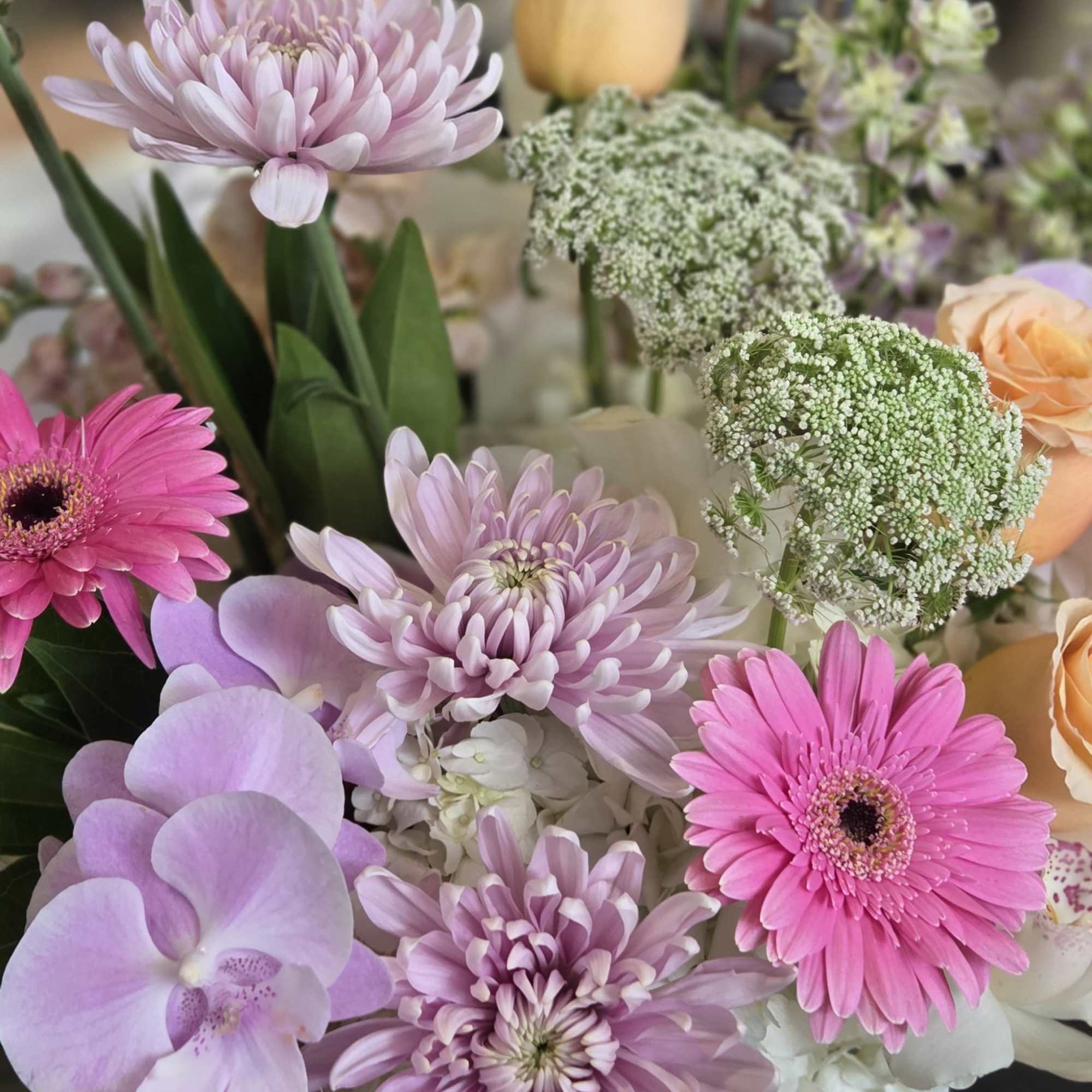 Pastel bouquet with pink gerbera daisies, lavender orchids, and chrysanthemums in a white vase.