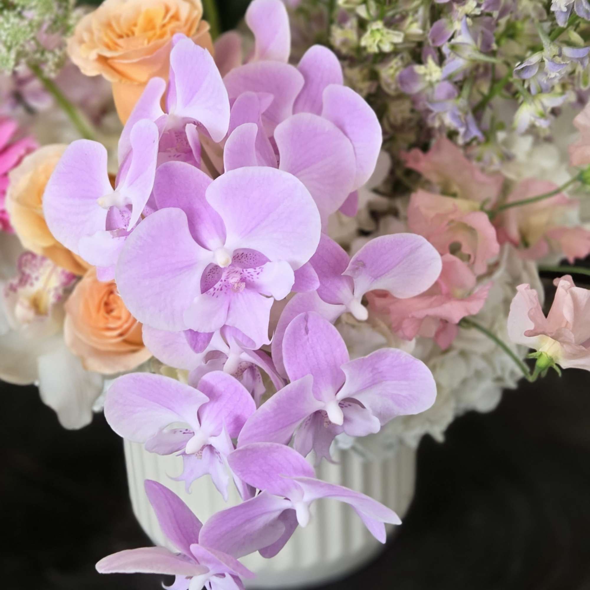 Lavender orchids and peach roses arranged in a white vase